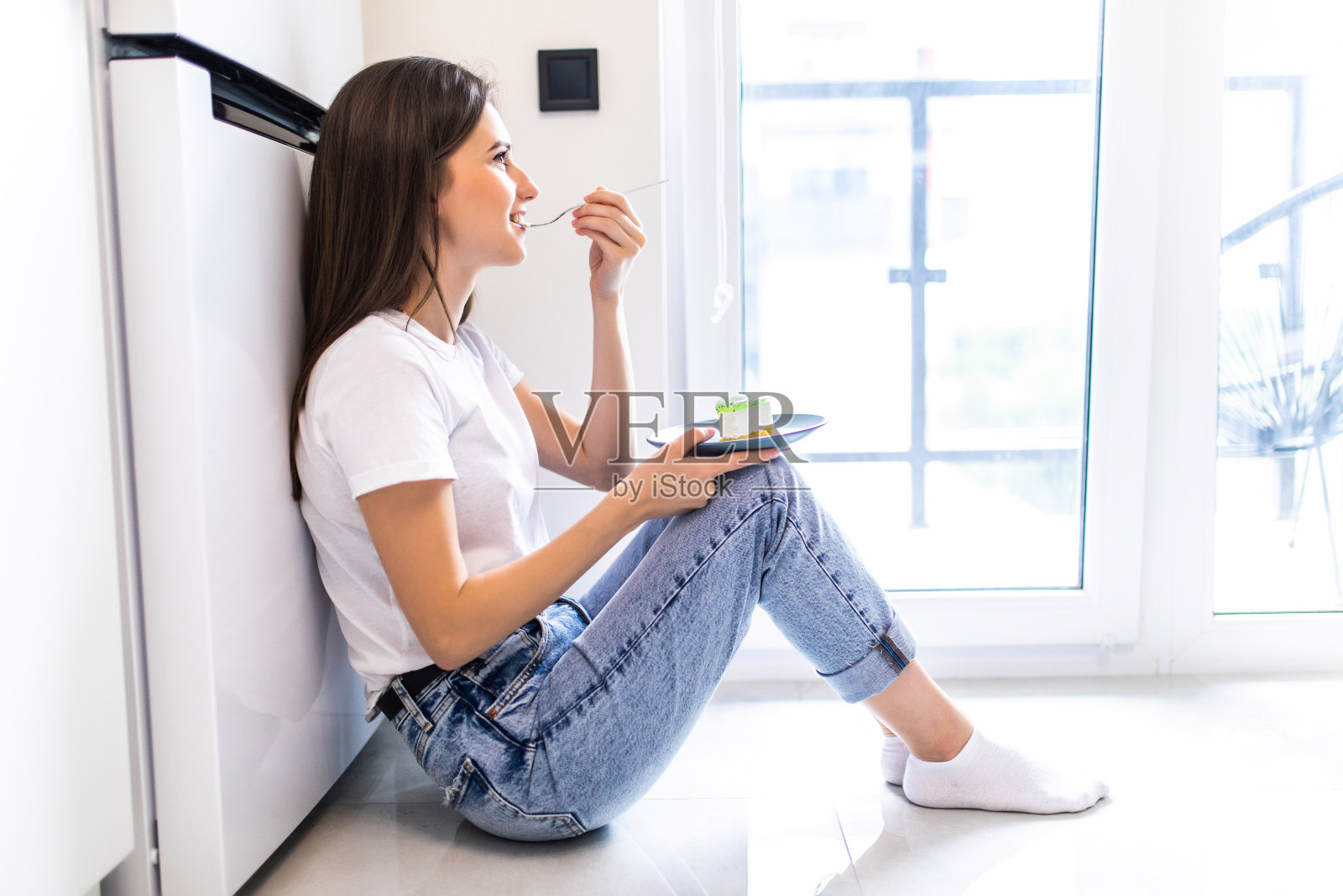 穿着休闲装的漂亮年轻女子坐在家里的地板上品尝美味的巧克力。照片摄影图片