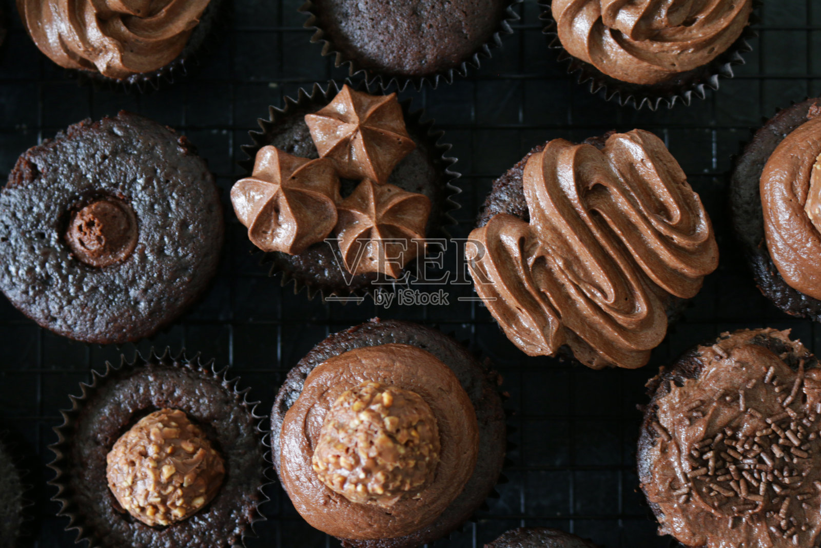 这是自制巧克力纸杯蛋糕的特写，上面覆盖着管道状的巧克力糖霜，金属冷却架上的黑色纸蛋糕盒，石板背景，高架景观照片摄影图片