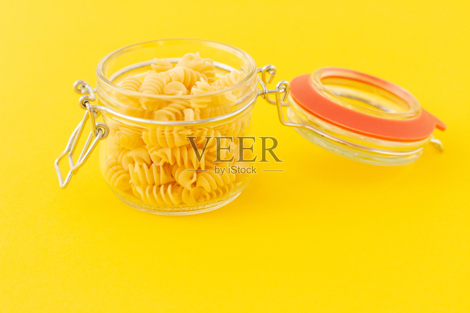 干燥的意大利螺旋面放在一个开着的玻璃罐子里，背景是黄色的。照片摄影图片