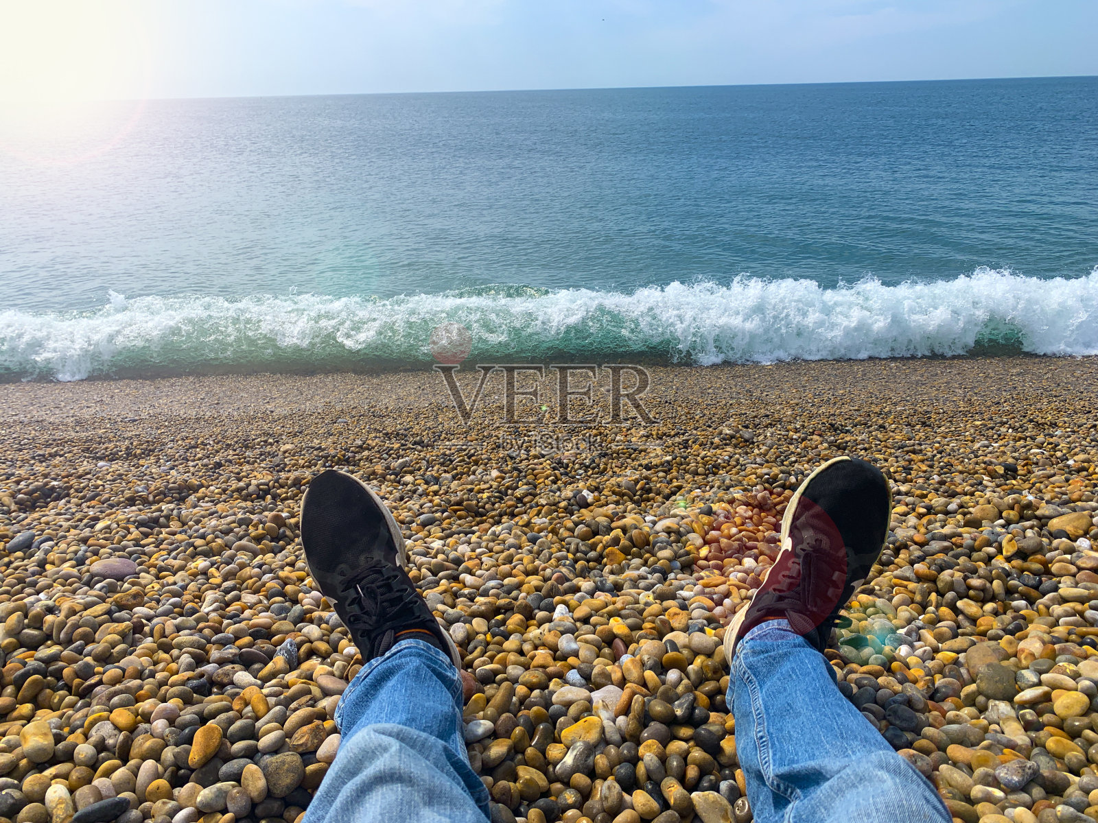 在一个阳光明媚的日子里，穿着牛仔裤坐在圆石滩上照片摄影图片