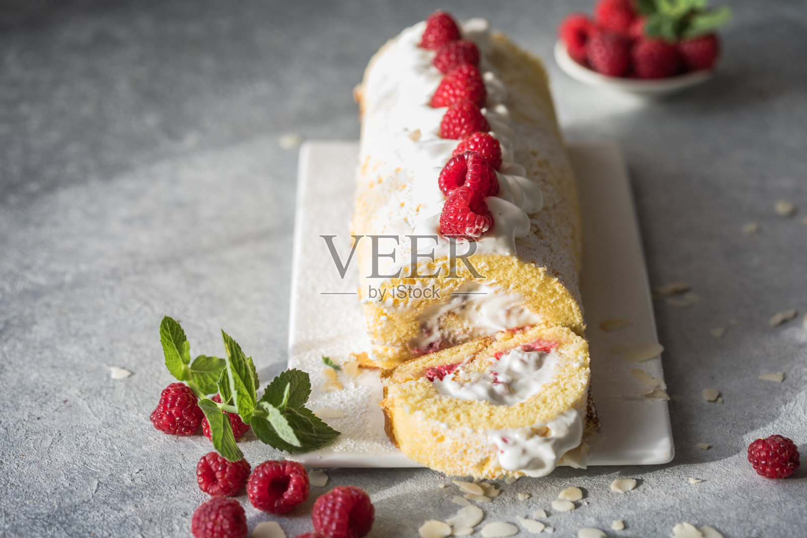 海绵蛋糕卷馅奶油和覆盆子，以白色的石头为背景。软的焦点。夏季食品的概念照片摄影图片