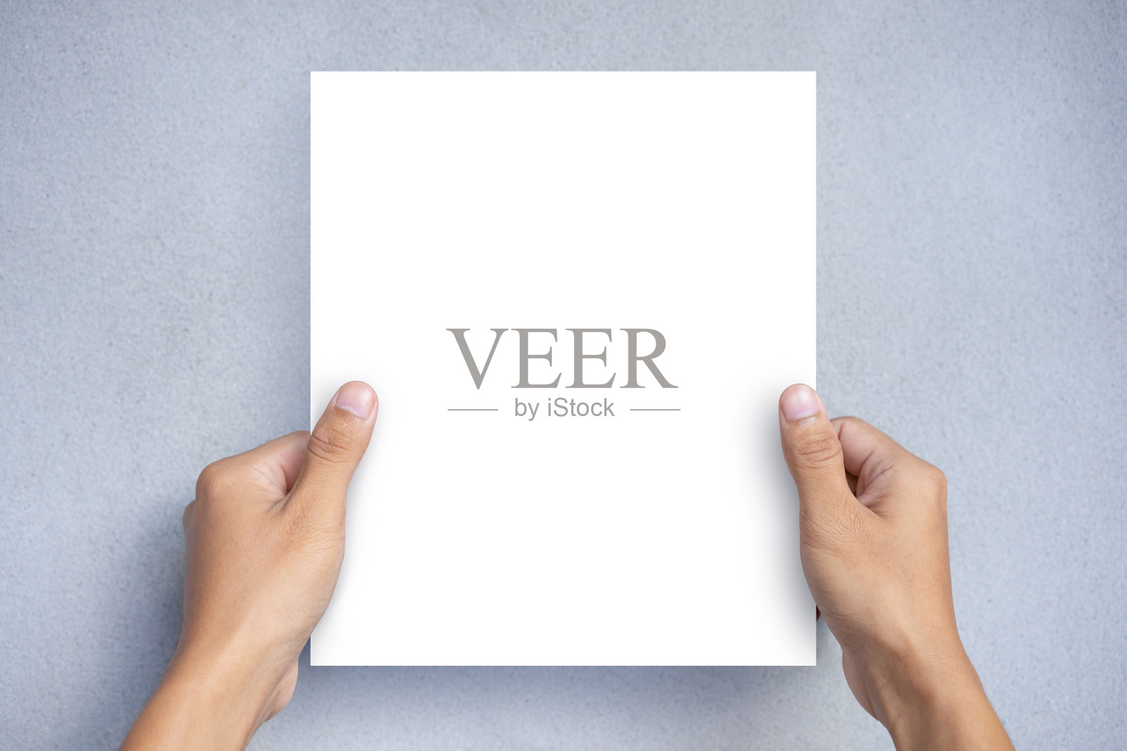 手拿一张空白的白纸模拟在一个灰色的背景。空白宣传册模板，传单照片摄影图片