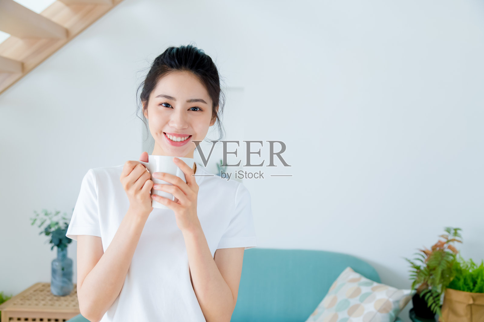 年轻的亚洲女人马尾辫在白色t恤拿一杯咖啡或茶放松在家里在早上。照片摄影图片