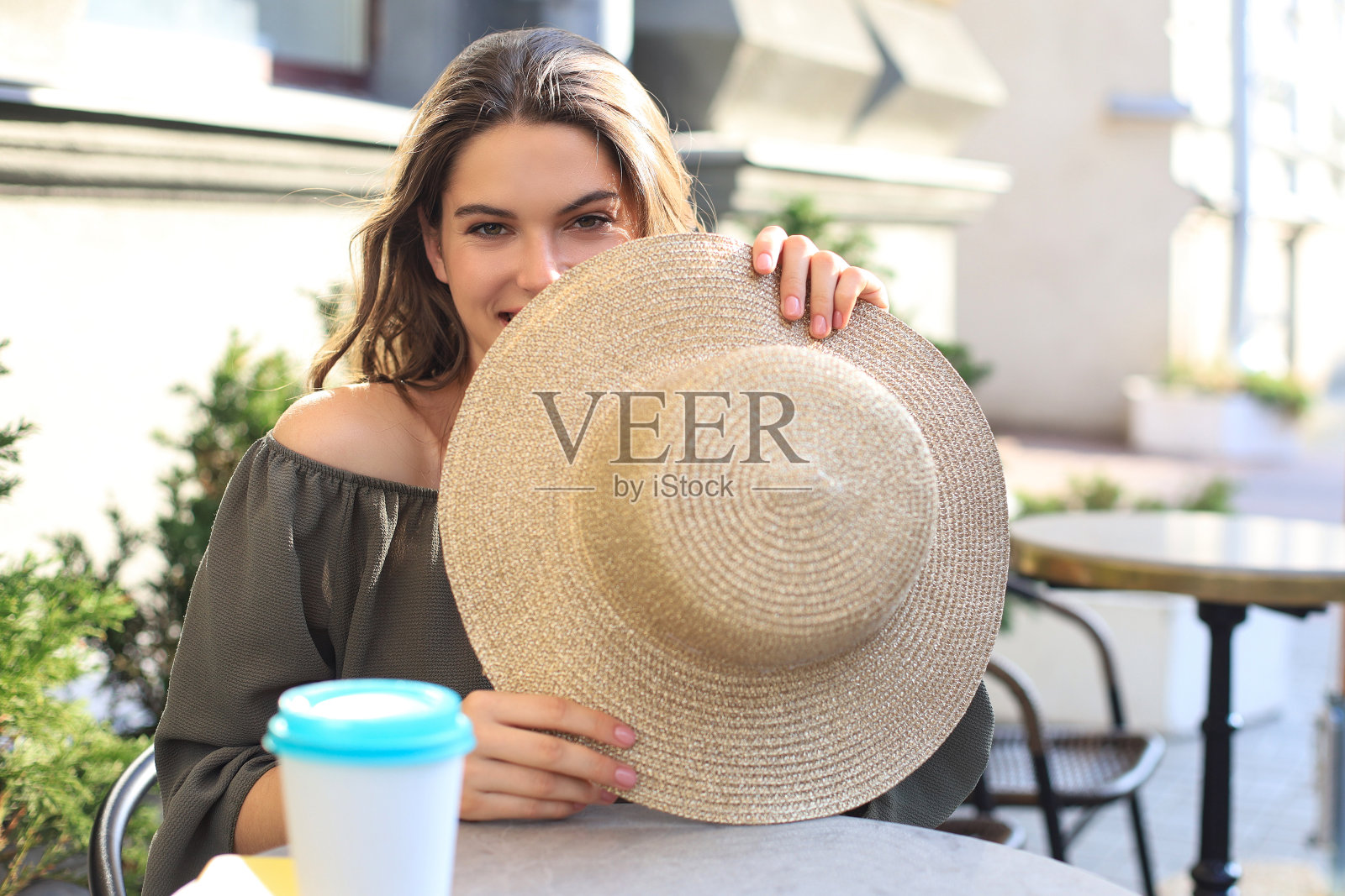 一个女孩的肖像，她的脸隐藏在一顶草帽后面，而坐在夏天的街头咖啡馆。照片摄影图片