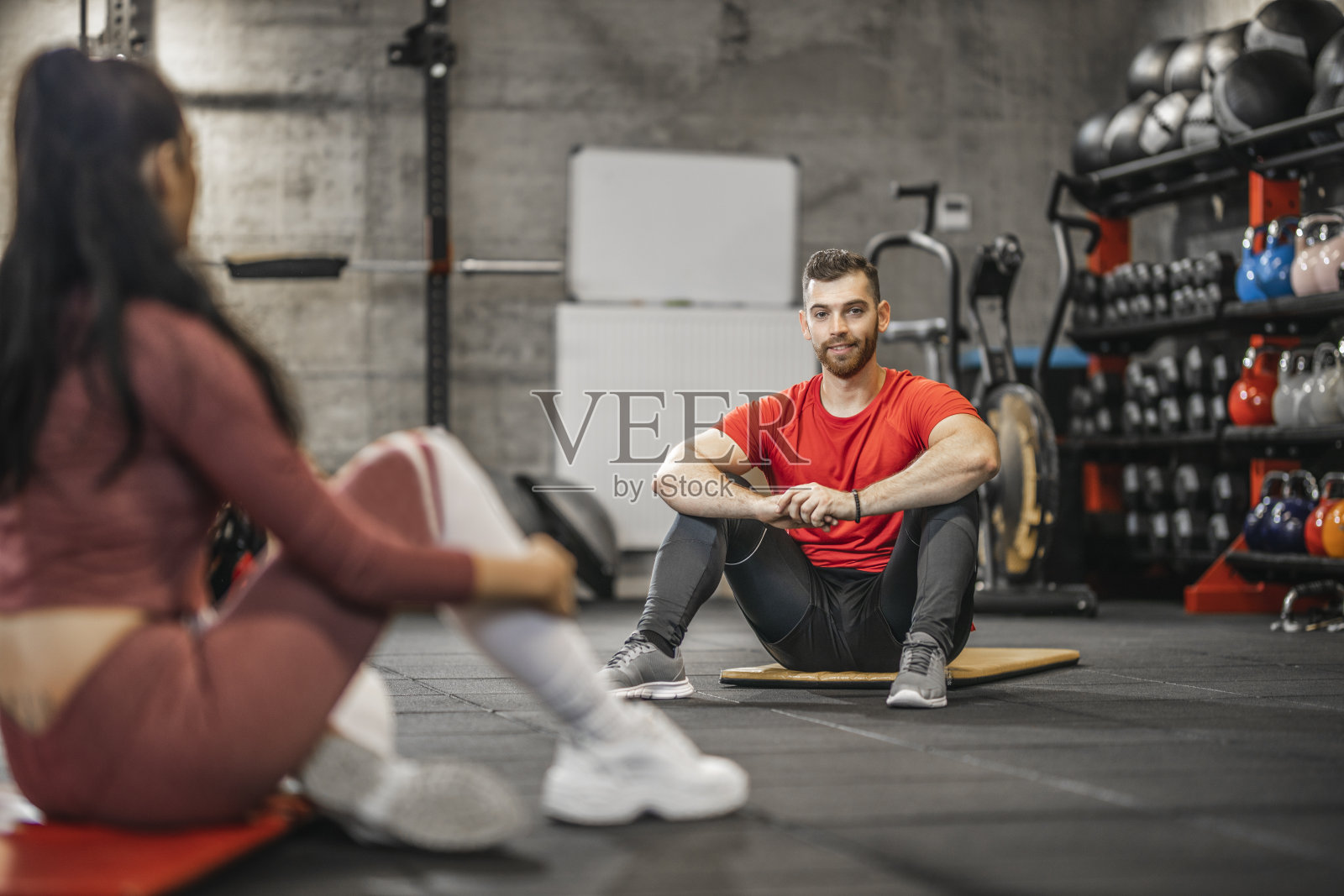在健身俱乐部，情侣们在运动训练后坐在运动垫上聊天休息照片摄影图片