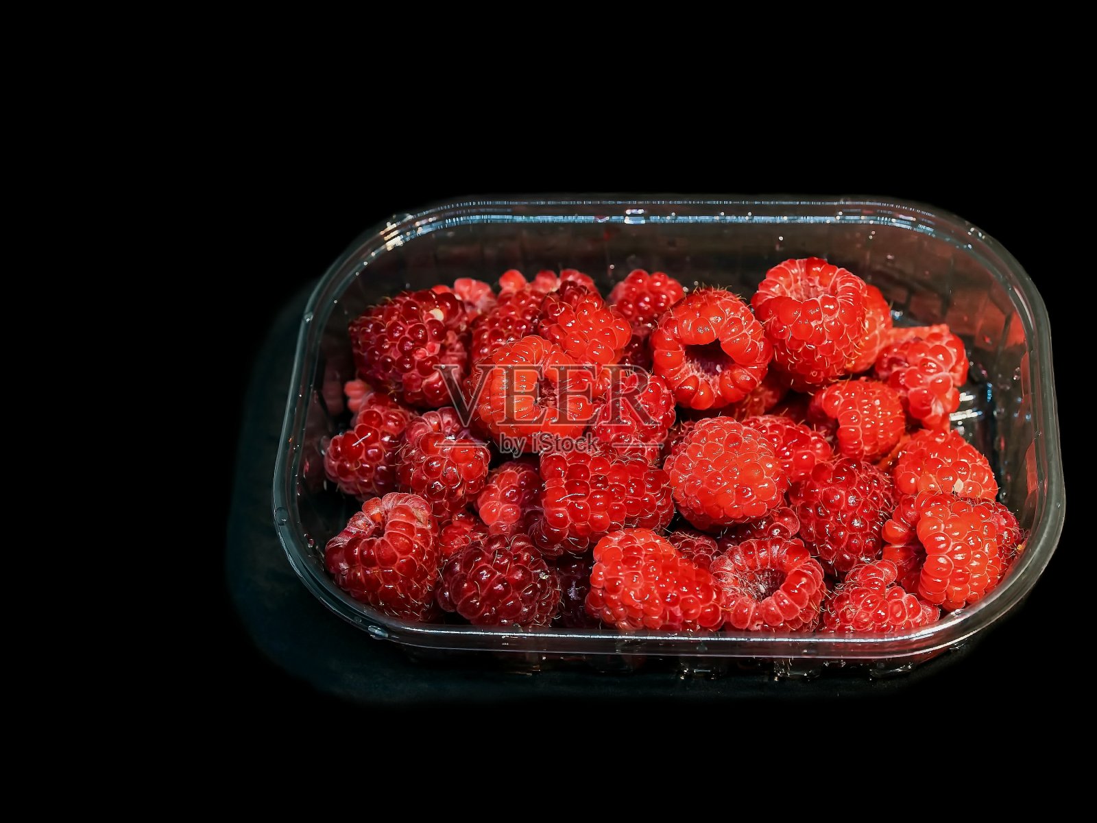 黑色背景上塑料盒装红色覆盆子照片摄影图片