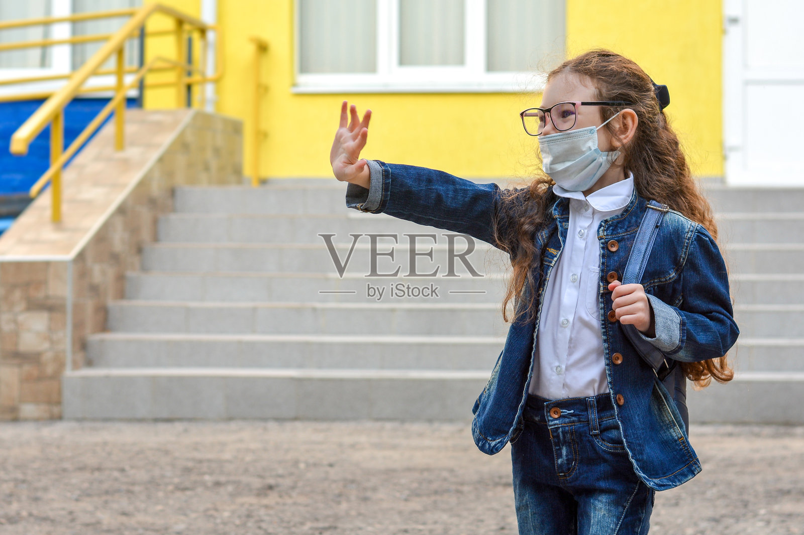 带着医用面具的女学生向我问好。社会距离。回到学校。大流行结束后孩子们在上学。保护儿童免受流感病毒感染的概念照片摄影图片