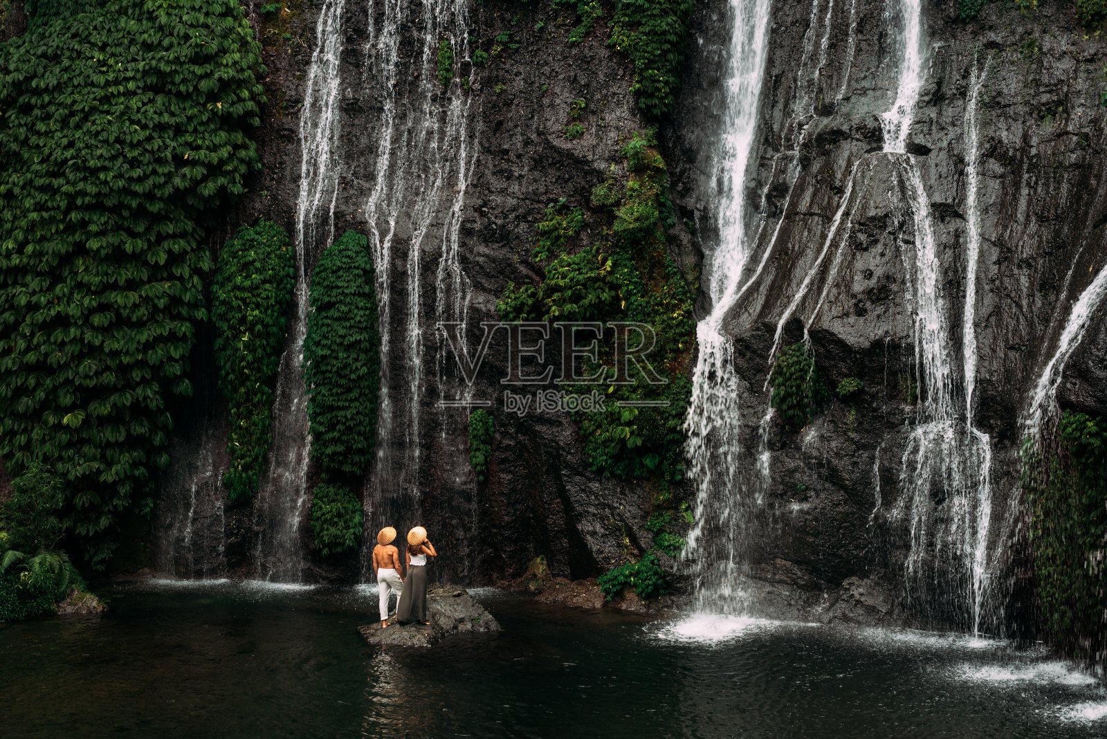 瀑布边的情侣，后视图。一对夫妇在印度尼西亚欣赏美丽的瀑布。一对情侣在巴厘岛度假。蜜月旅行。这对夫妇正在亚洲旅行。副本的空间。印尼之旅照片摄影图片