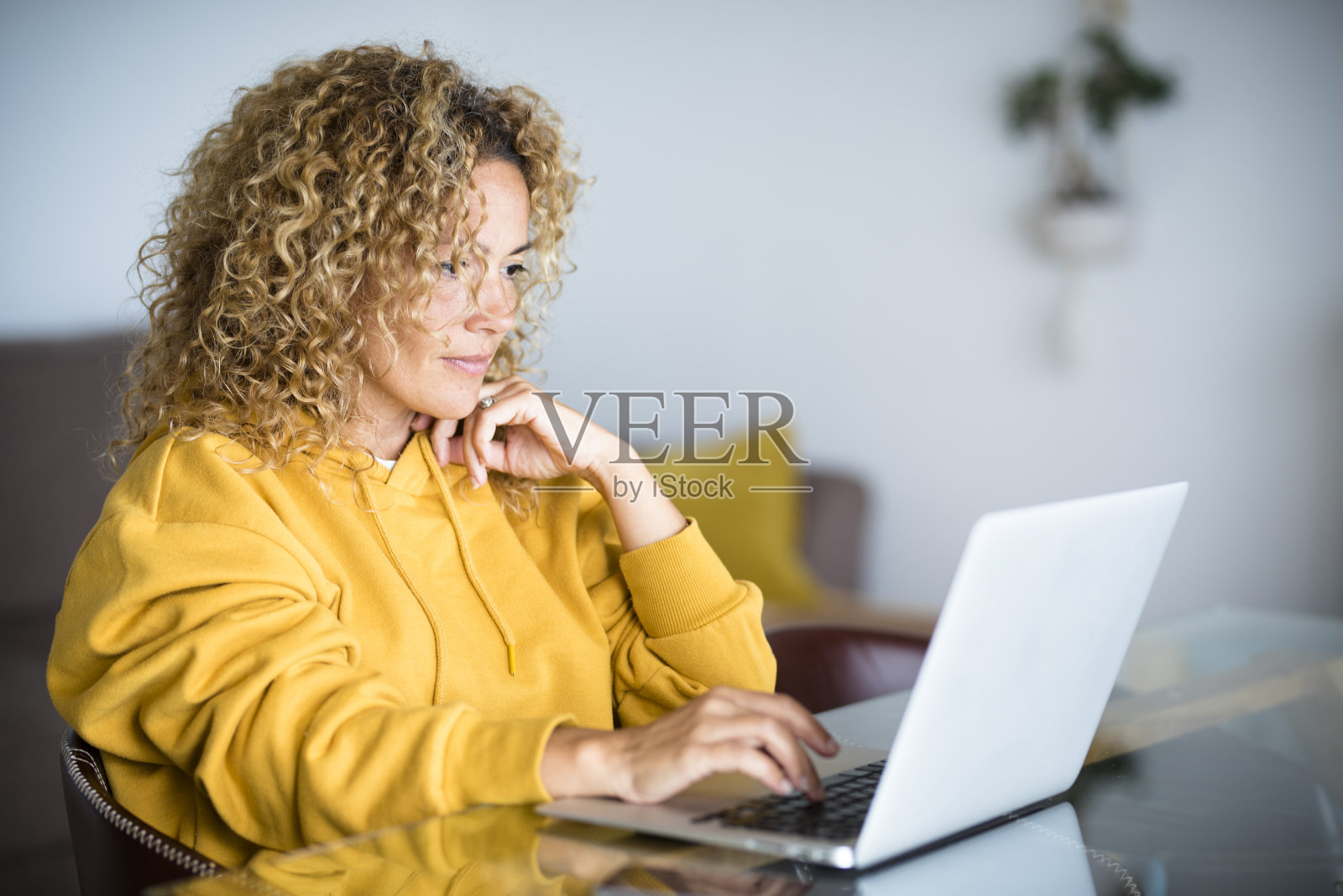 美丽的中年现代女性工作在电脑笔记本电脑在家里坐在桌子-数字智能工作的概念与互联网技术和替代办公室求职的概念照片摄影图片