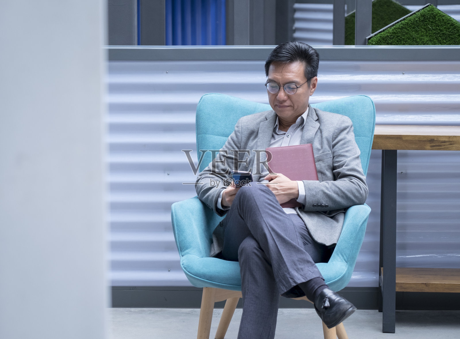 一位中国商人坐在绿色的椅子上看手机照片摄影图片