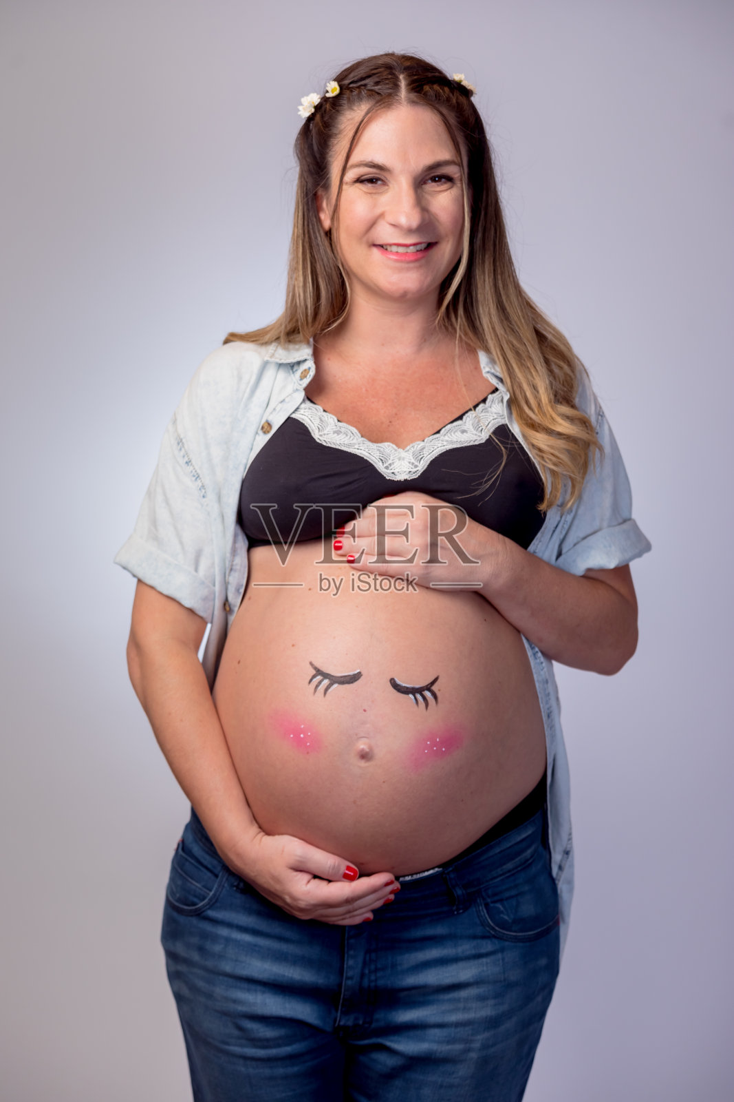 在白色背景下，孕妇的肚子上画着一张温柔的脸照片摄影图片