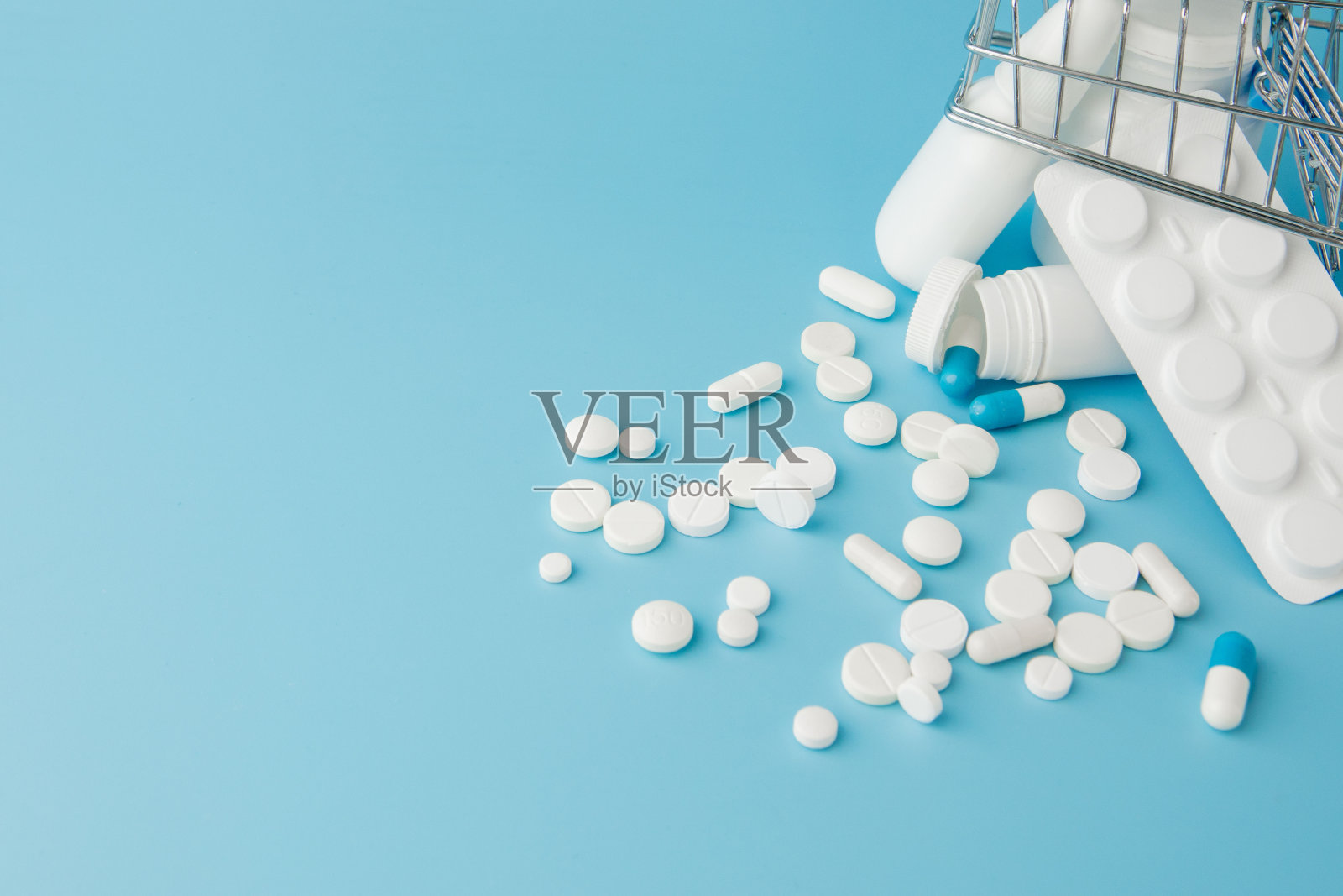 蓝色背景上散落着各种药片、药品、喷雾、瓶子、温度计、注射器和空的购物车。药房购物的概念照片摄影图片