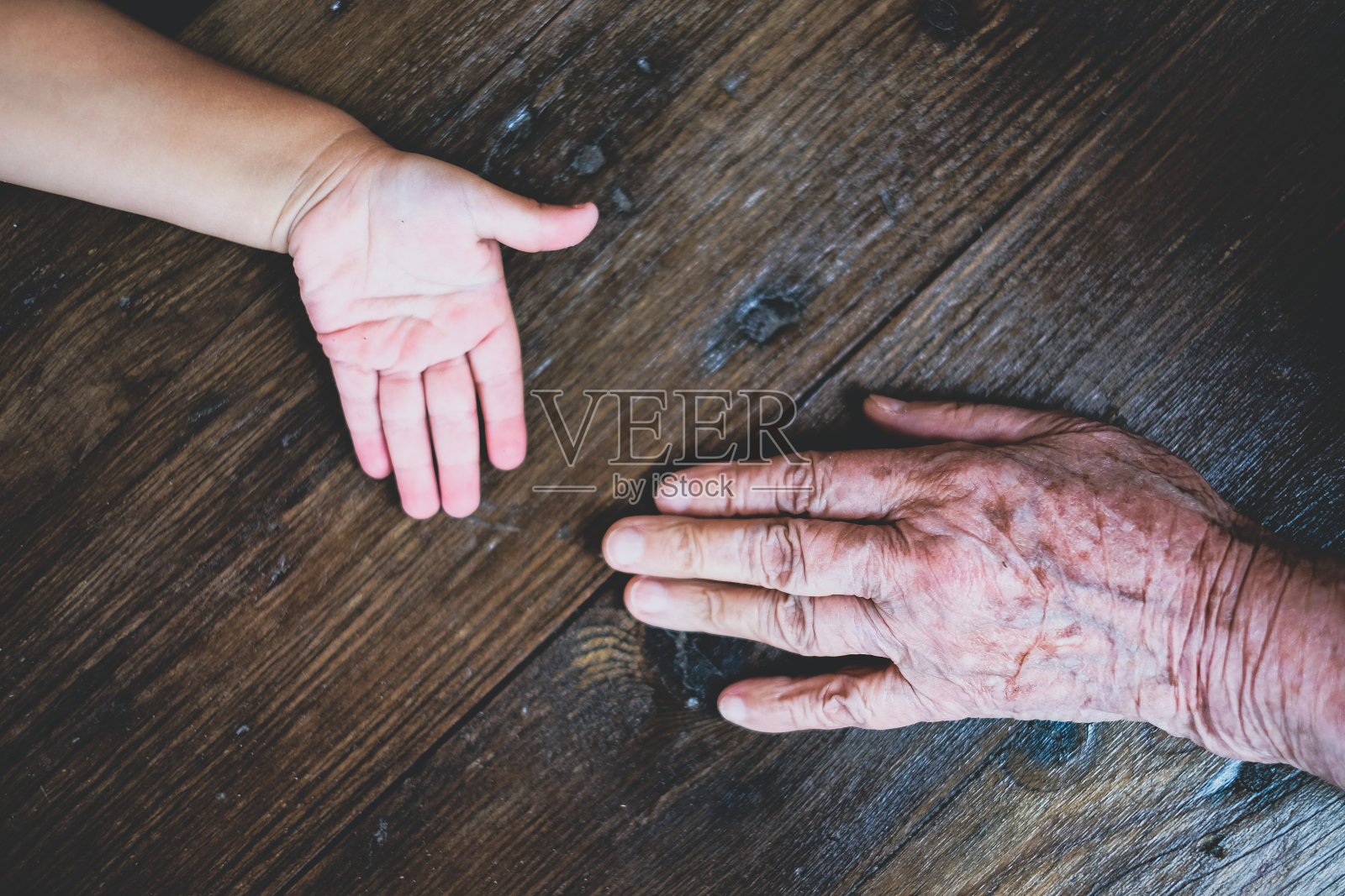 曾祖母和蹒跚学步的孩子的手放在一张木桌上照片摄影图片