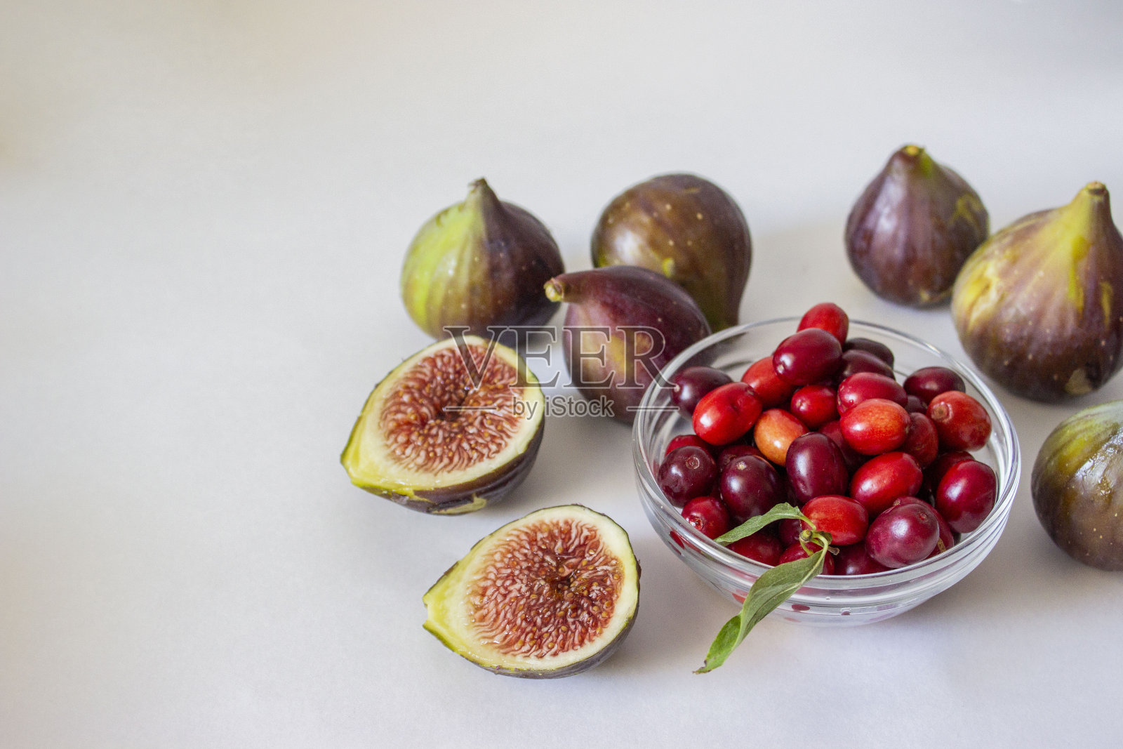 成熟的无花果，紫绿色，整个果实，切成带籽的红色果肉。山茱萸在一个玻璃碗灰色和蓝色的背景。照片摄影图片