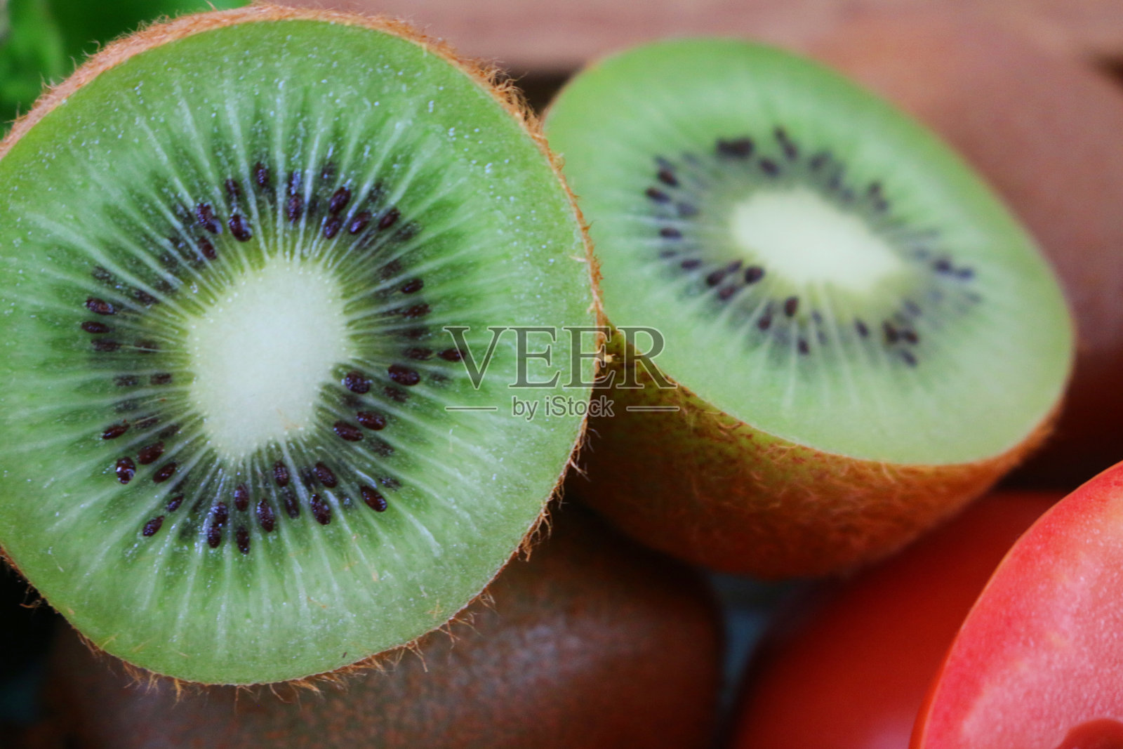 猕猴桃(中国猕猴桃)的特写图像切成两半显示模糊的棕色皮肤和亮绿色的果肉与一圈黑色的种子，模糊的水果和蔬菜背景照片摄影图片
