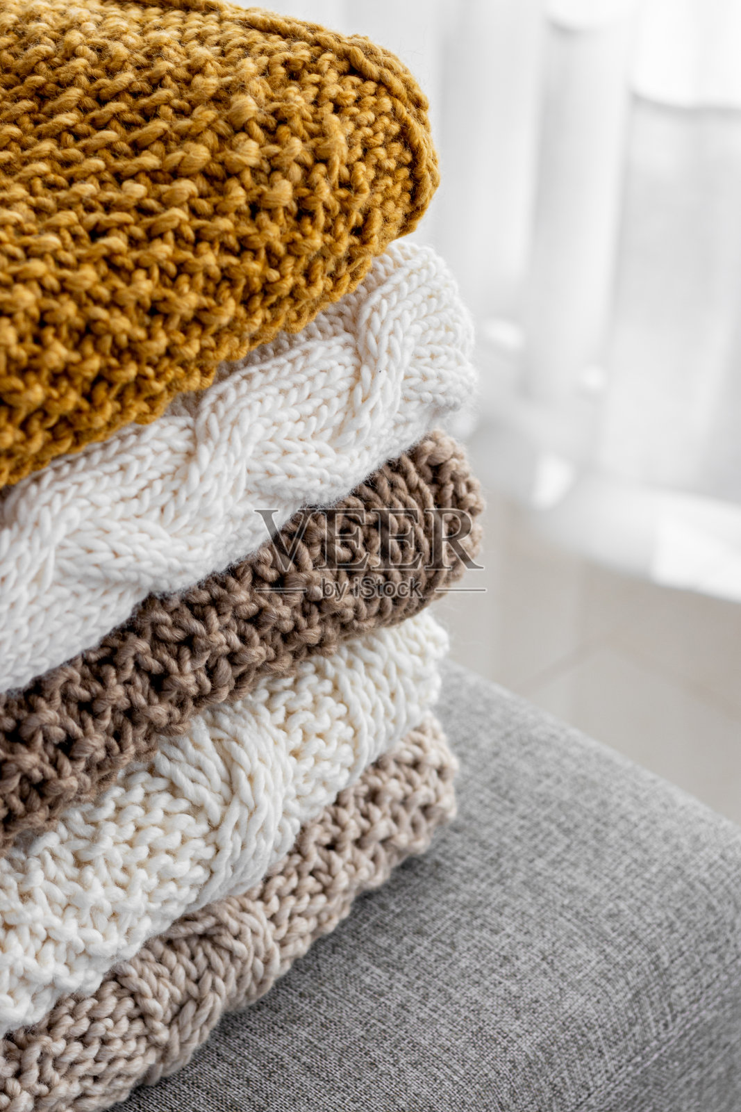 细部堆叠着米色、棕色、白色五种不同颜色的毛毯，手工编织在灰色扶手椅上。照片摄影图片