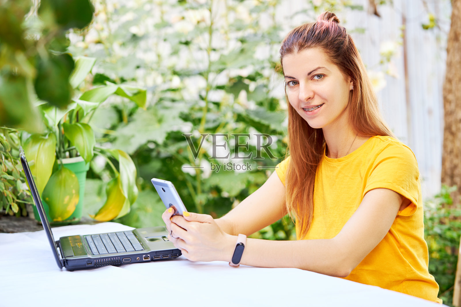年轻女子在户外使用智能手机，以绿色环境为背景。远程工作。自由职业者和电子学习生活方式概念照片摄影图片