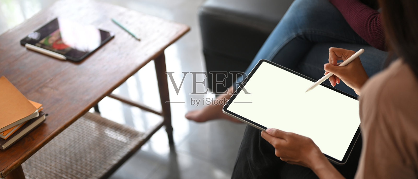 一张裁剪过的图片显示，一位女士正在黑色沙发上使用一台白色的空白屏幕平板电脑。照片摄影图片