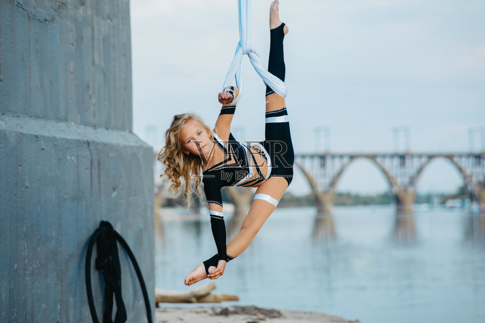 小女孩在悬挂的空中丝绸上表演体操劈开。照片摄影图片