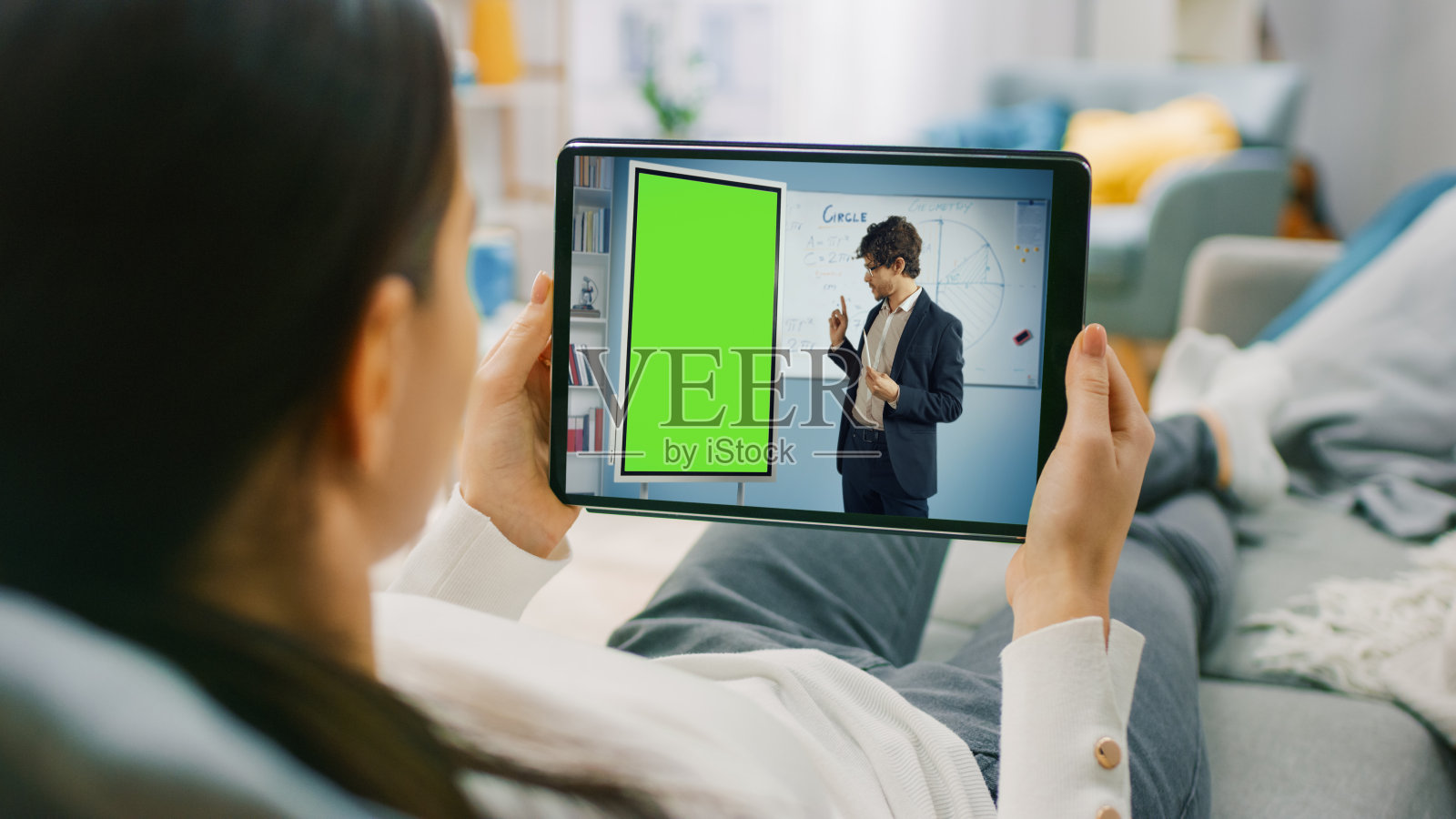 年轻女子在家里使用平板电脑在水平横向肖像模式与她的老师视频通话。教师使用绿屏模板讲解题目。照片摄影图片