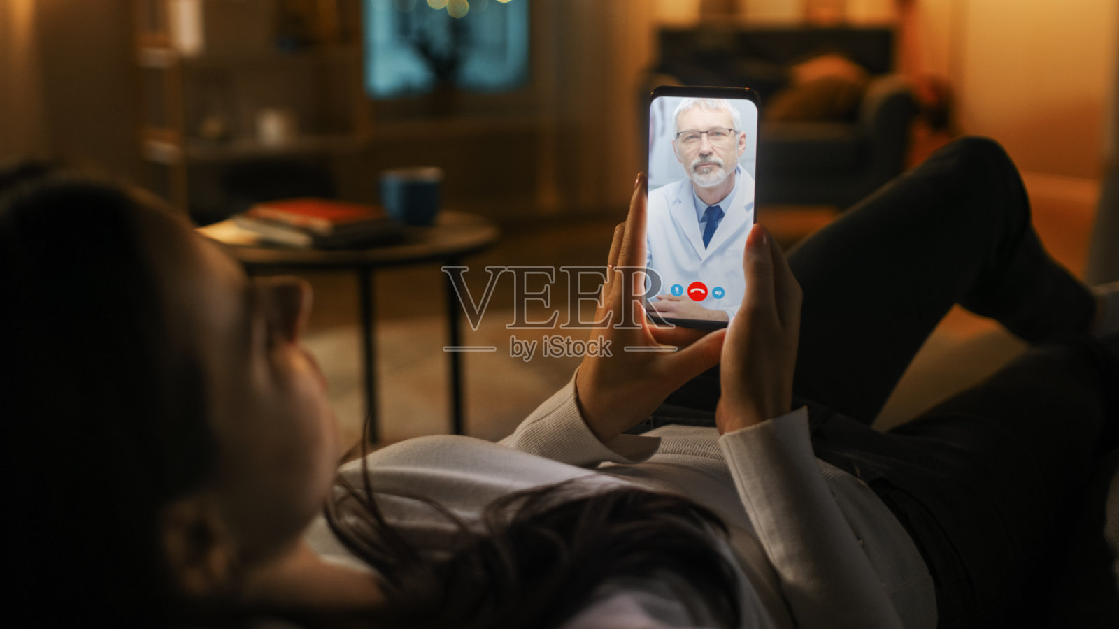 女孩在家病了，用智能手机通过视频会议和医生聊天。美丽的女人用在线视频聊天应用和专业医生聊天。深夜照片摄影图片