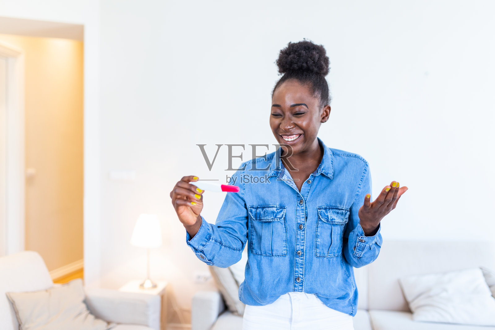 年轻女子高兴地看着验孕棒。终于怀孕了。迷人的黑人女性坐在家里的沙发上微笑着看着验孕棒照片摄影图片