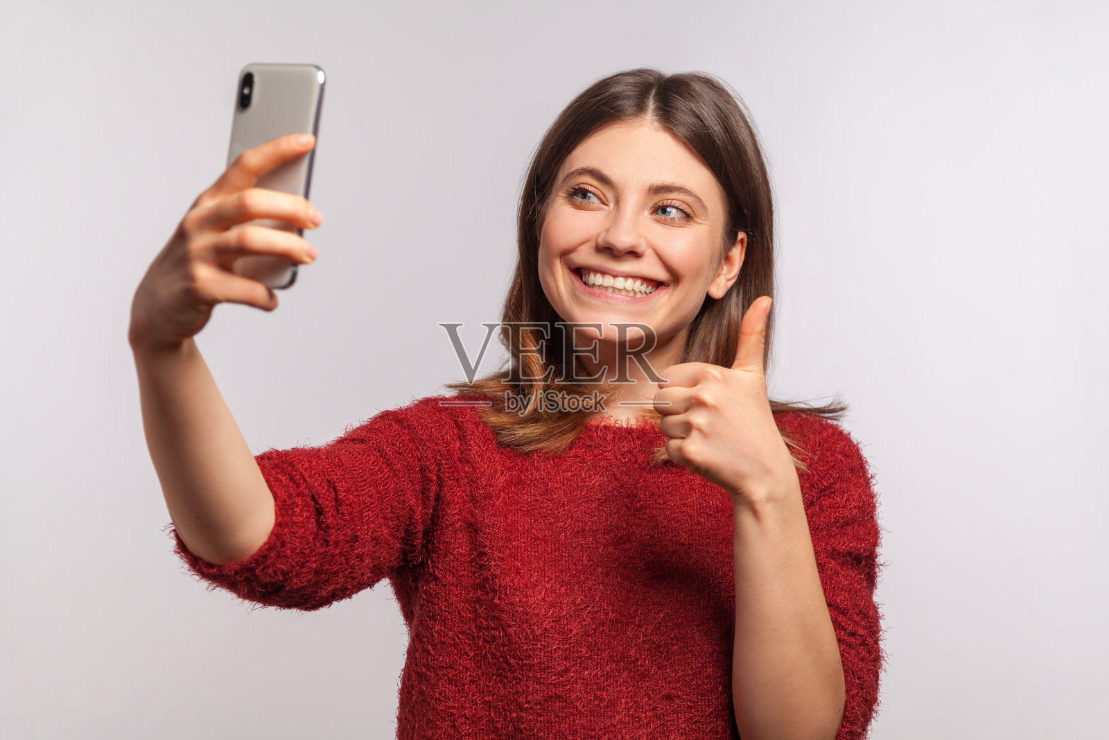 友好的女孩穿着毛茸茸的毛衣，通过手机进行视频通话，竖起大拇指，交流照片摄影图片