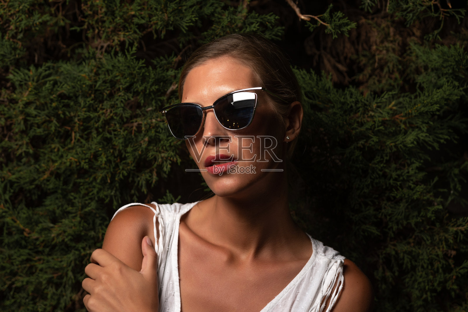 美丽的女人在一个白色的裙子摆姿势在树叶的背景。时尚的概念。硬光。照片摄影图片