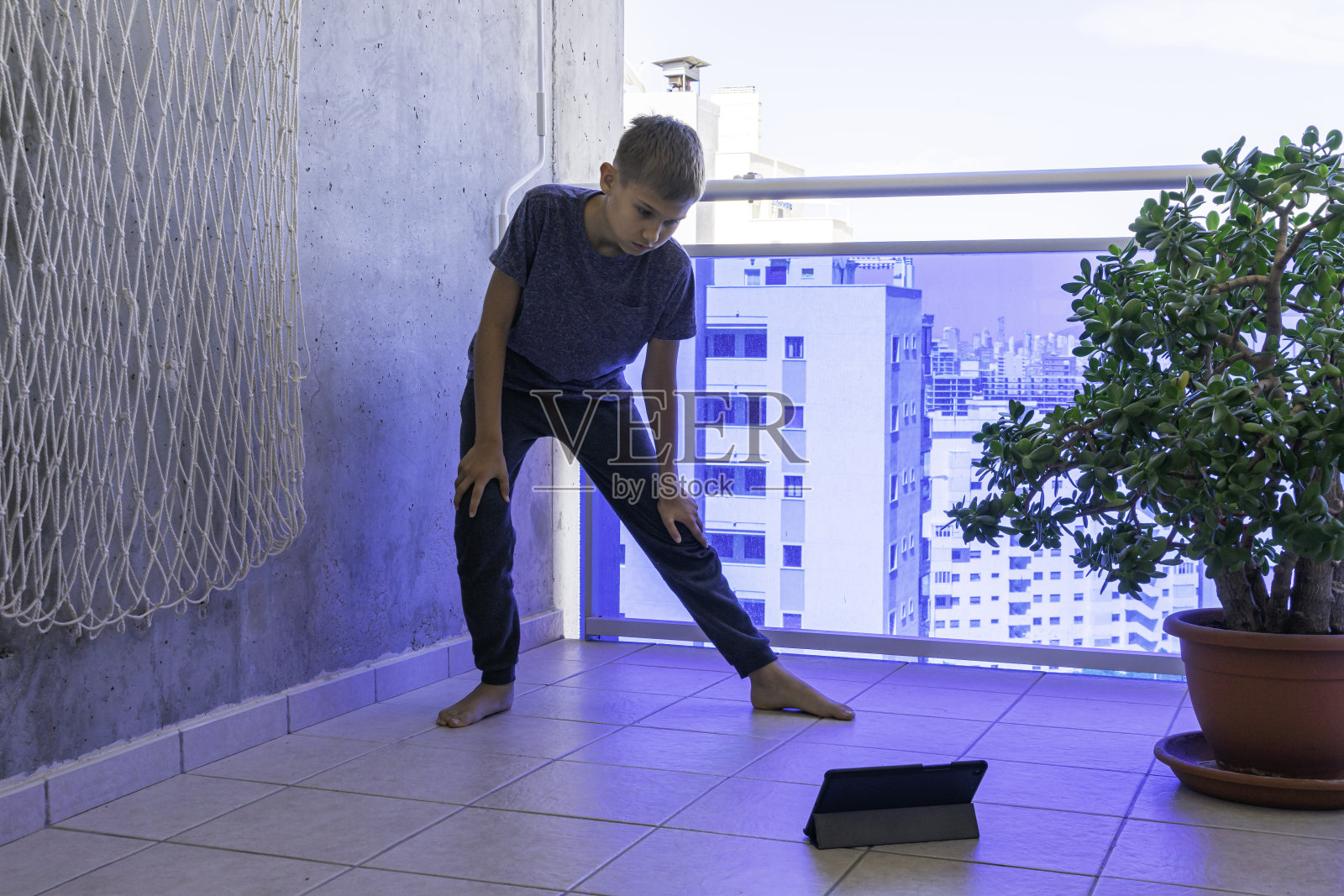 孩子拿着平板电脑在阳台上做运动。运动，健康的生活方式，积极的休闲在家照片摄影图片