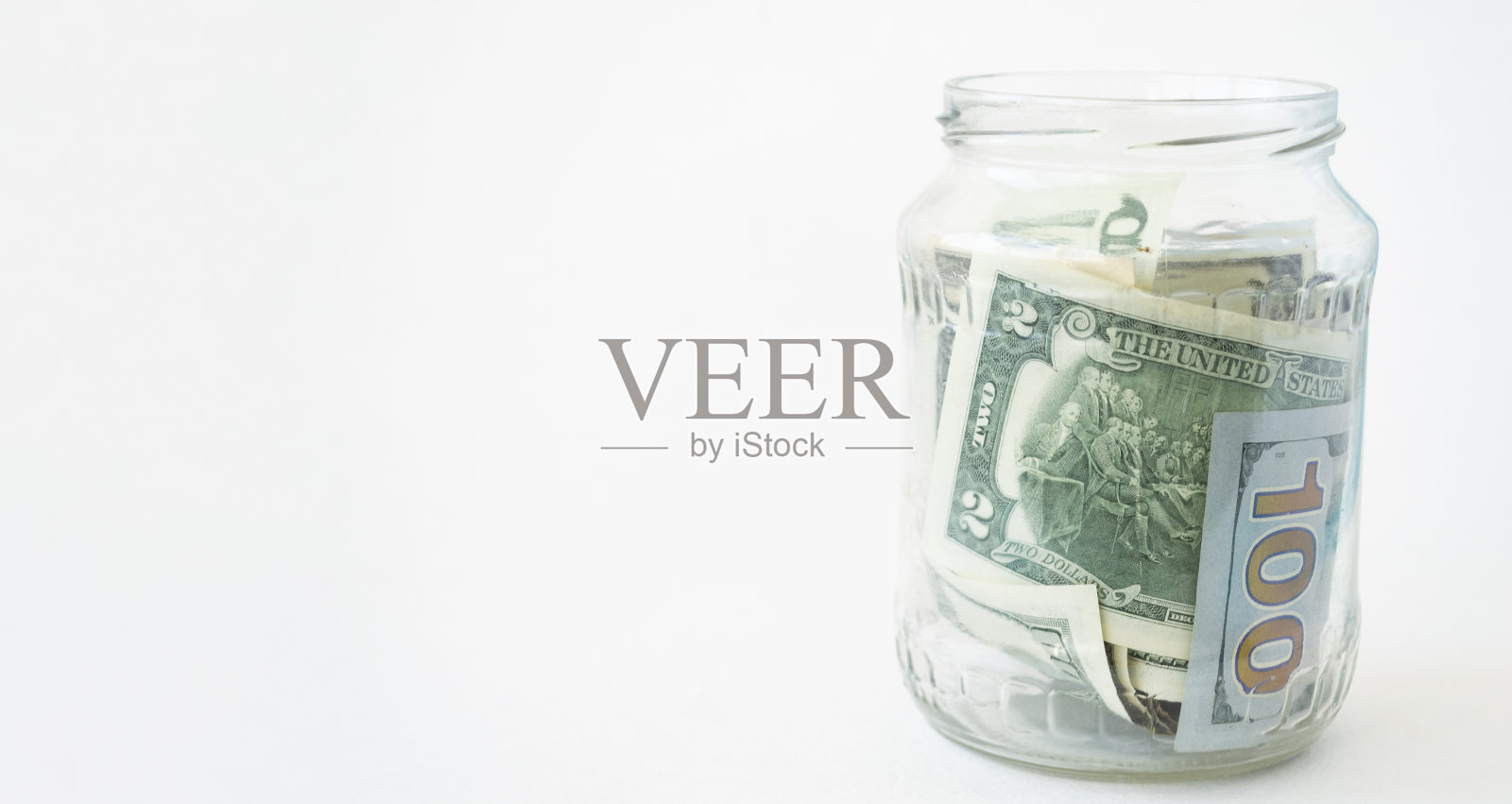 在白色的背景下，从一个玻璃罐里取出的存钱罐，里面装着生活用的新美元。副本的空间。经济的概念照片摄影图片