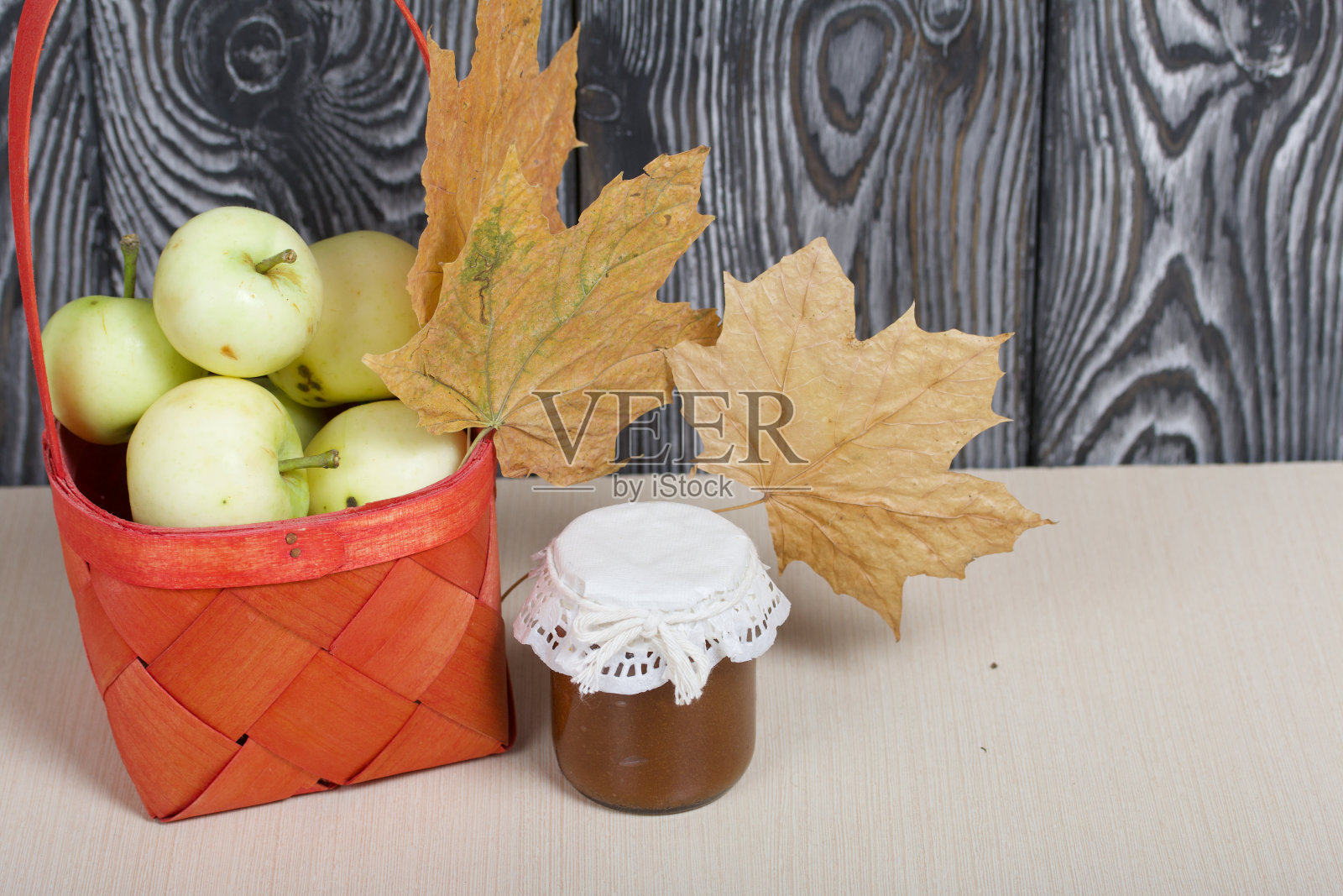 红柳条篮子里的苹果。罐子里的果酱、苹果和干枫叶就在附近。水果的收成。照片摄影图片