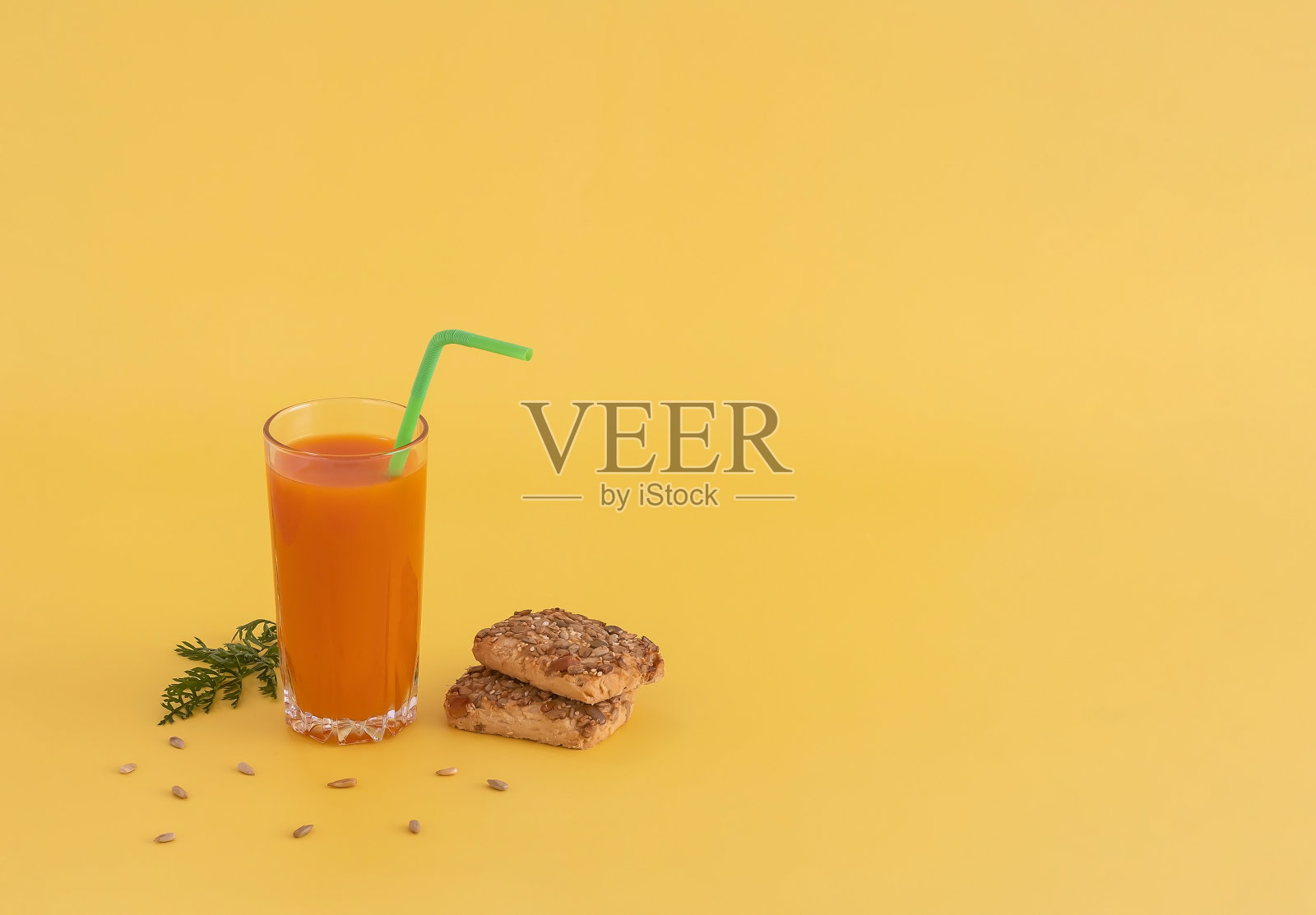 一杯有鸡尾酒管的胡萝卜汁和黄色背景上有种子和芝麻的饼干照片摄影图片