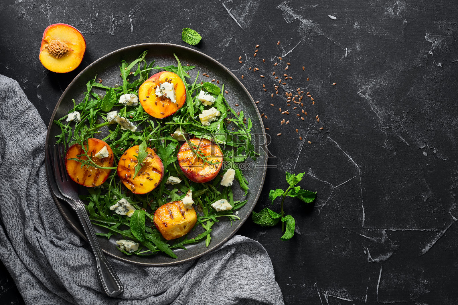 新鲜的饮食沙拉，烤桃子，芝麻菜和蓝奶酪在一个盘子在黑色的石头背景。素食和素食午餐或晚餐。俯视图，平放照片摄影图片