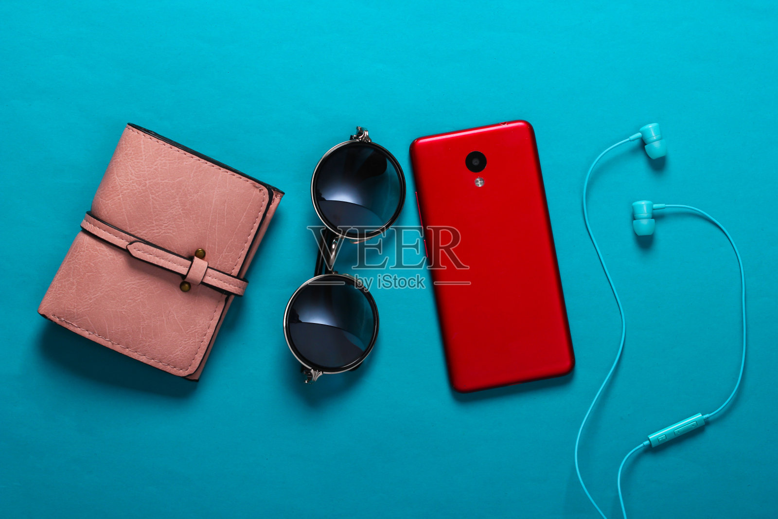女士的配件和小玩意的背景。耳机，时尚的圆形太阳镜，智能手机，蓝色背景的钱包。俯视图照片摄影图片