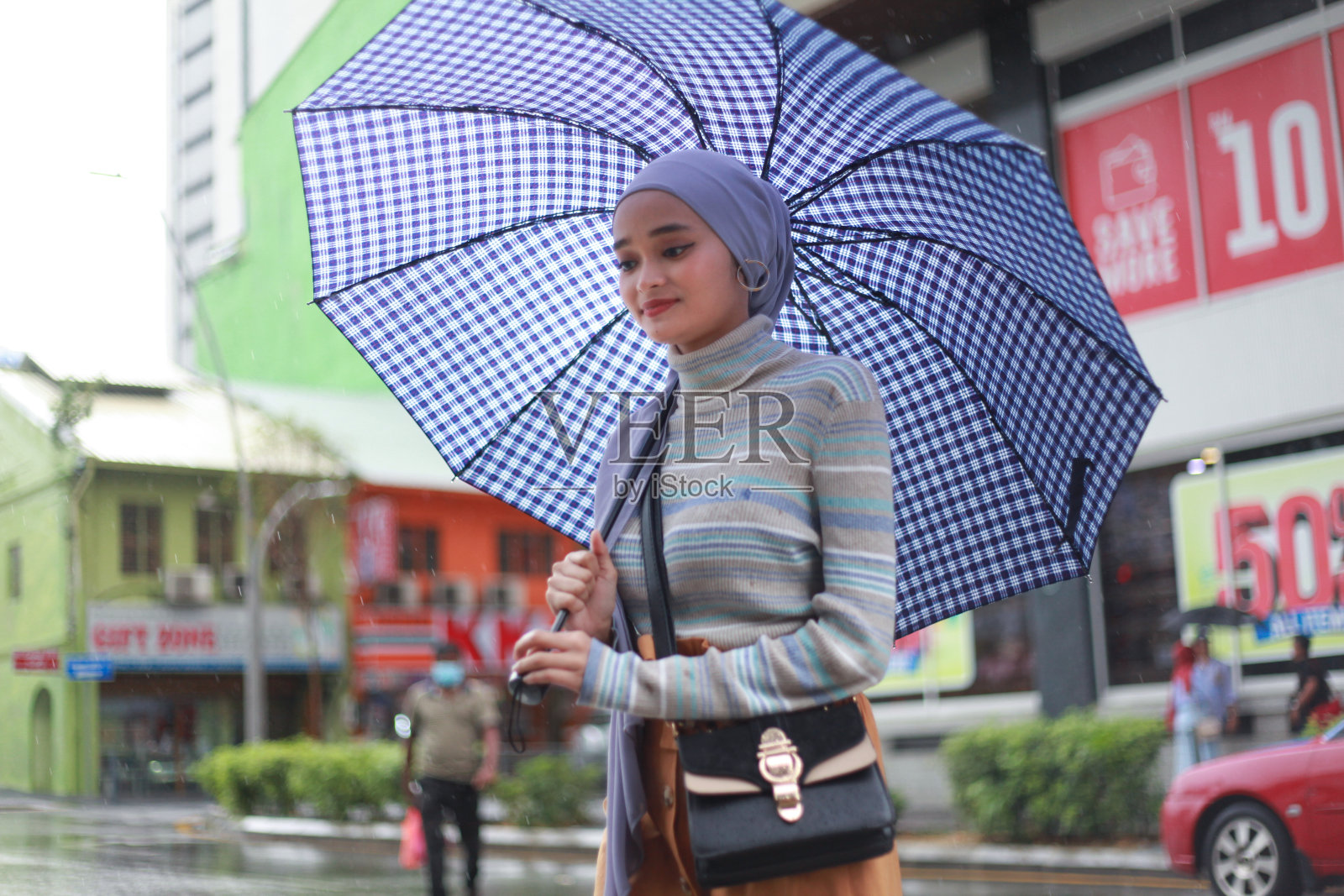 一位戴着头巾、撑着伞的穆斯林马来妇女在雨中行走照片摄影图片