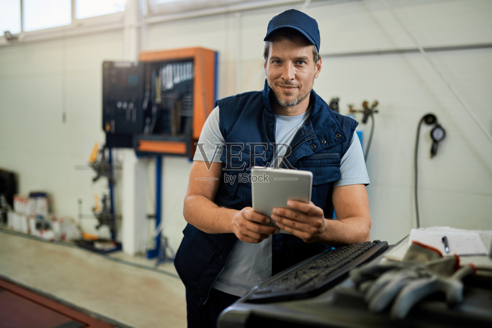 快乐的技工使用触摸板，而工作在汽车修理店。照片摄影图片