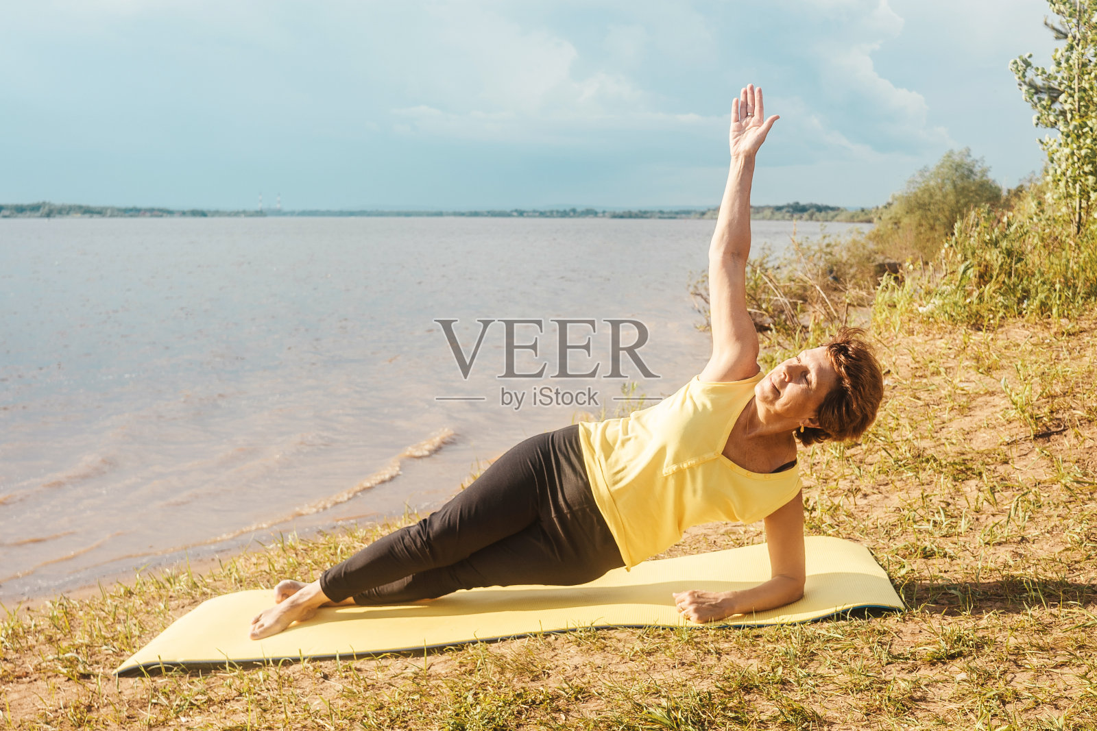 老妇人在河边做瑜伽。照片摄影图片