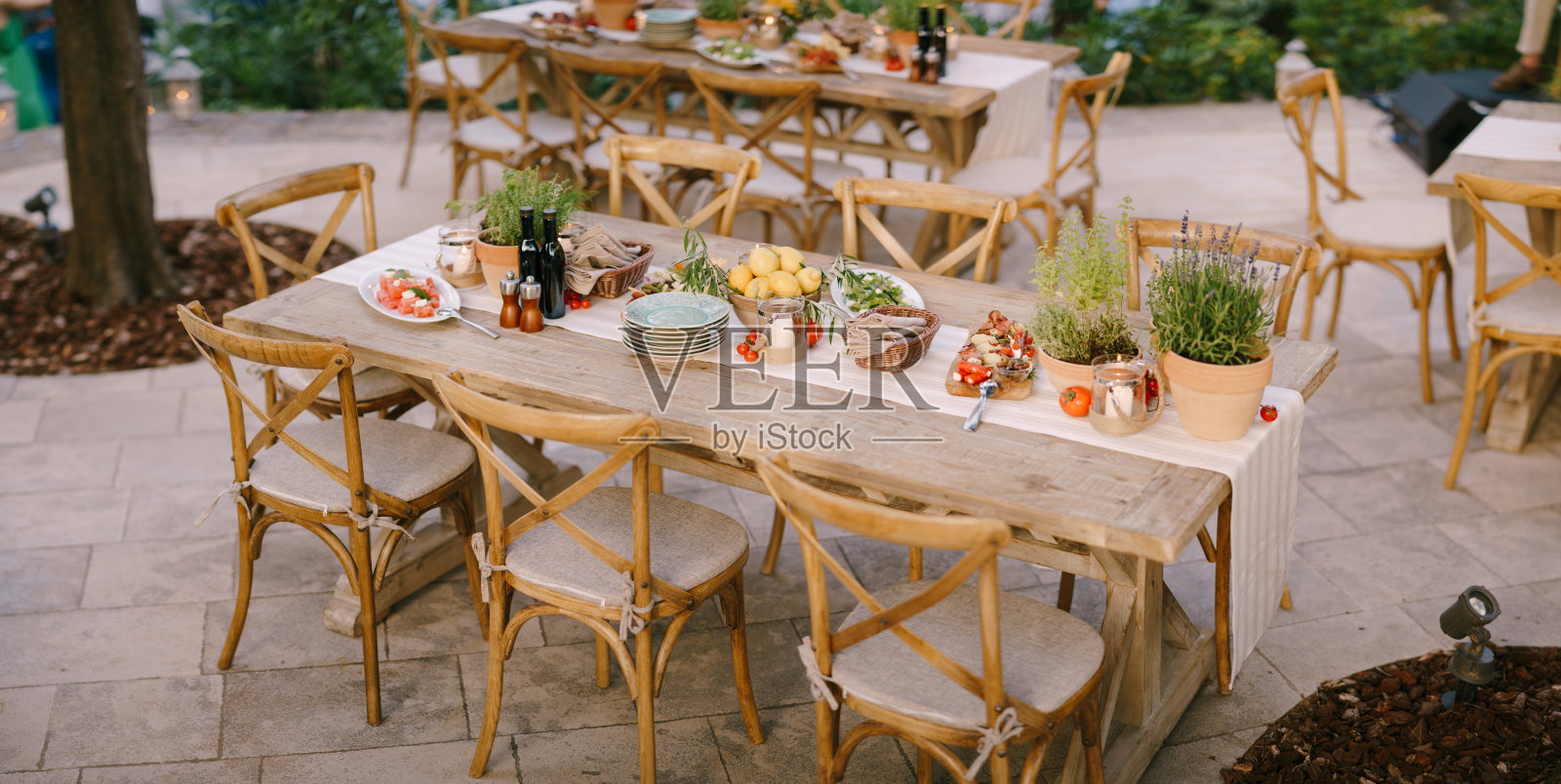 一个节日桌子上的鲜花在盆中，在一个开放的区域和树木。乡村风格的木椅，自助餐桌上的小吃。照片摄影图片