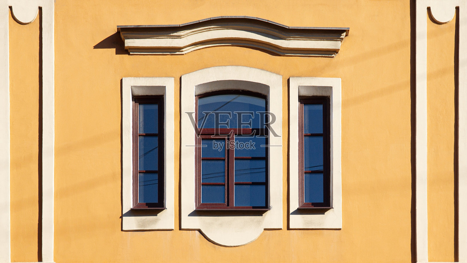 棕色的旧三扇窗户，白色的框架和山墙在黄色的墙壁上照片摄影图片