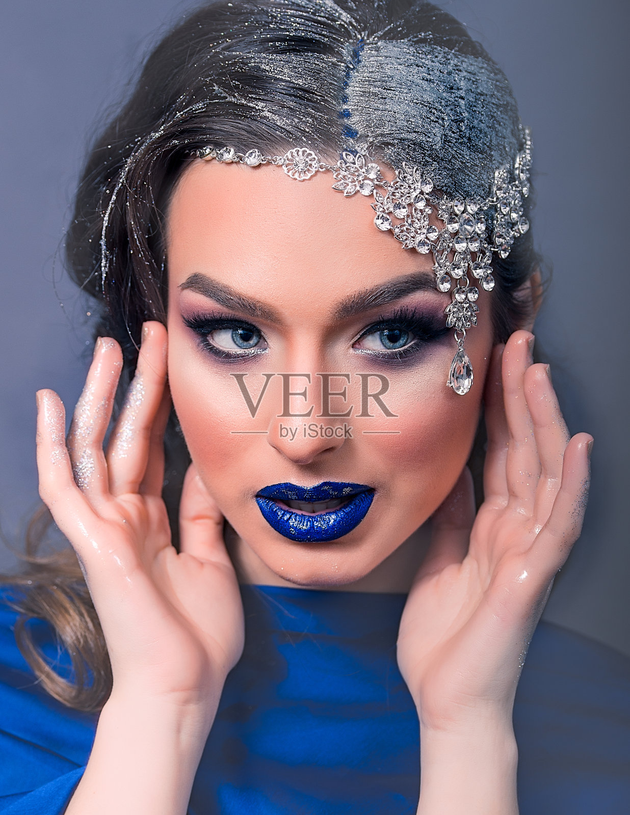 年轻的白人妇女与银饰和蓝嘴唇的特写。她戴着一个水晶白色的项链在她的头和她有她的头发漆成银色，在灰色的背景照片摄影图片