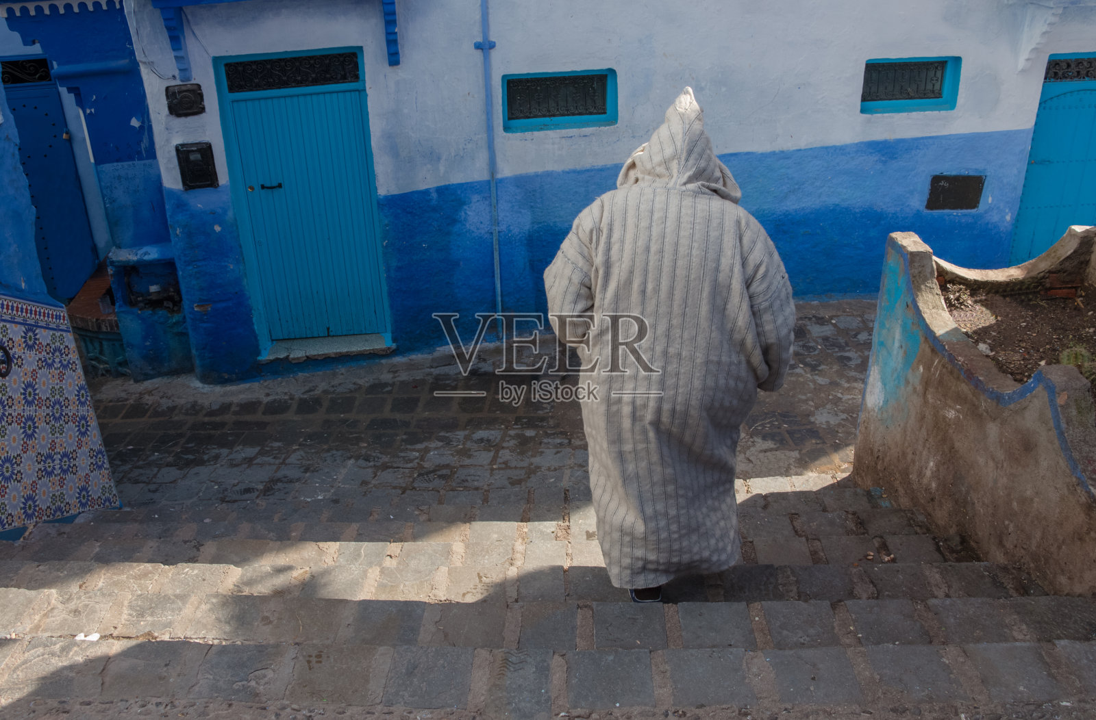 一位身穿传统摩洛哥jillaba的老人走在摩洛哥蓝色小镇Chefchaouen的蓝色街道上照片摄影图片