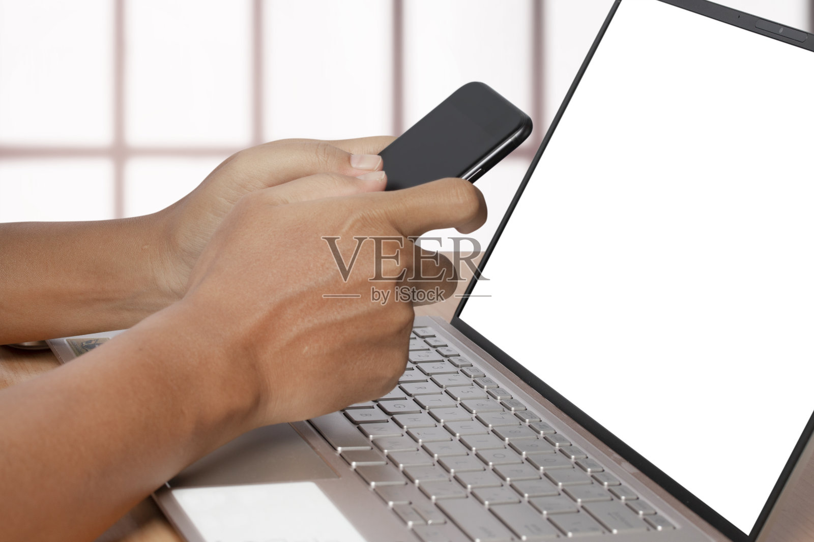 一名男子在室内使用智能手机和笔记本电脑。照片摄影图片