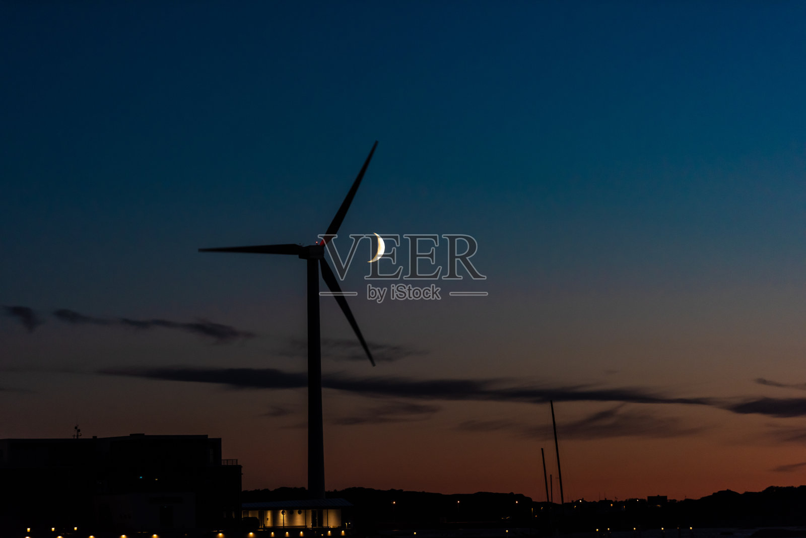 一弯新月在夜晚从风力涡轮机后面经过照片摄影图片