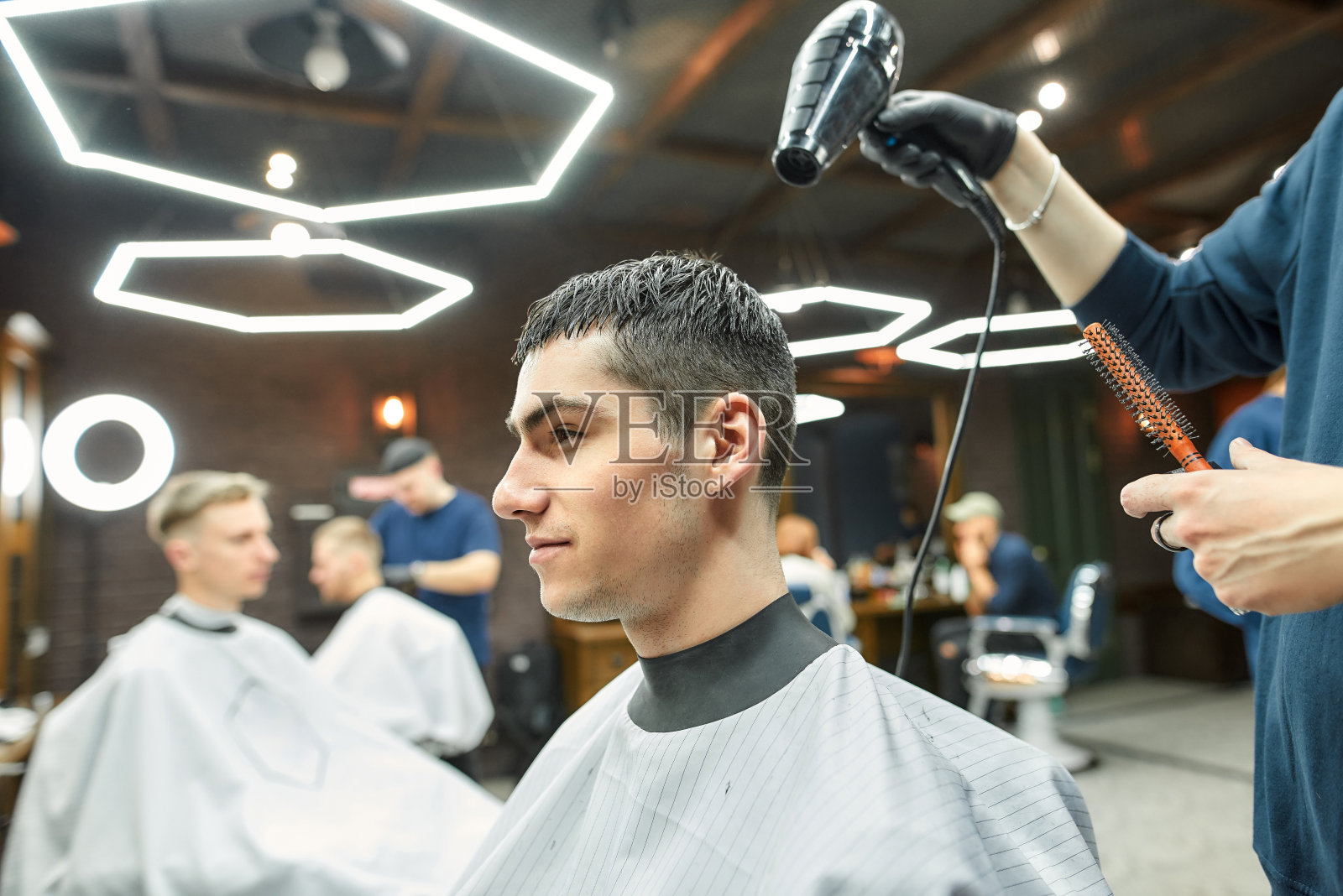 工作过程。在现代化的理发店里，一个理发师正在吹一个帅哥的头发照片摄影图片