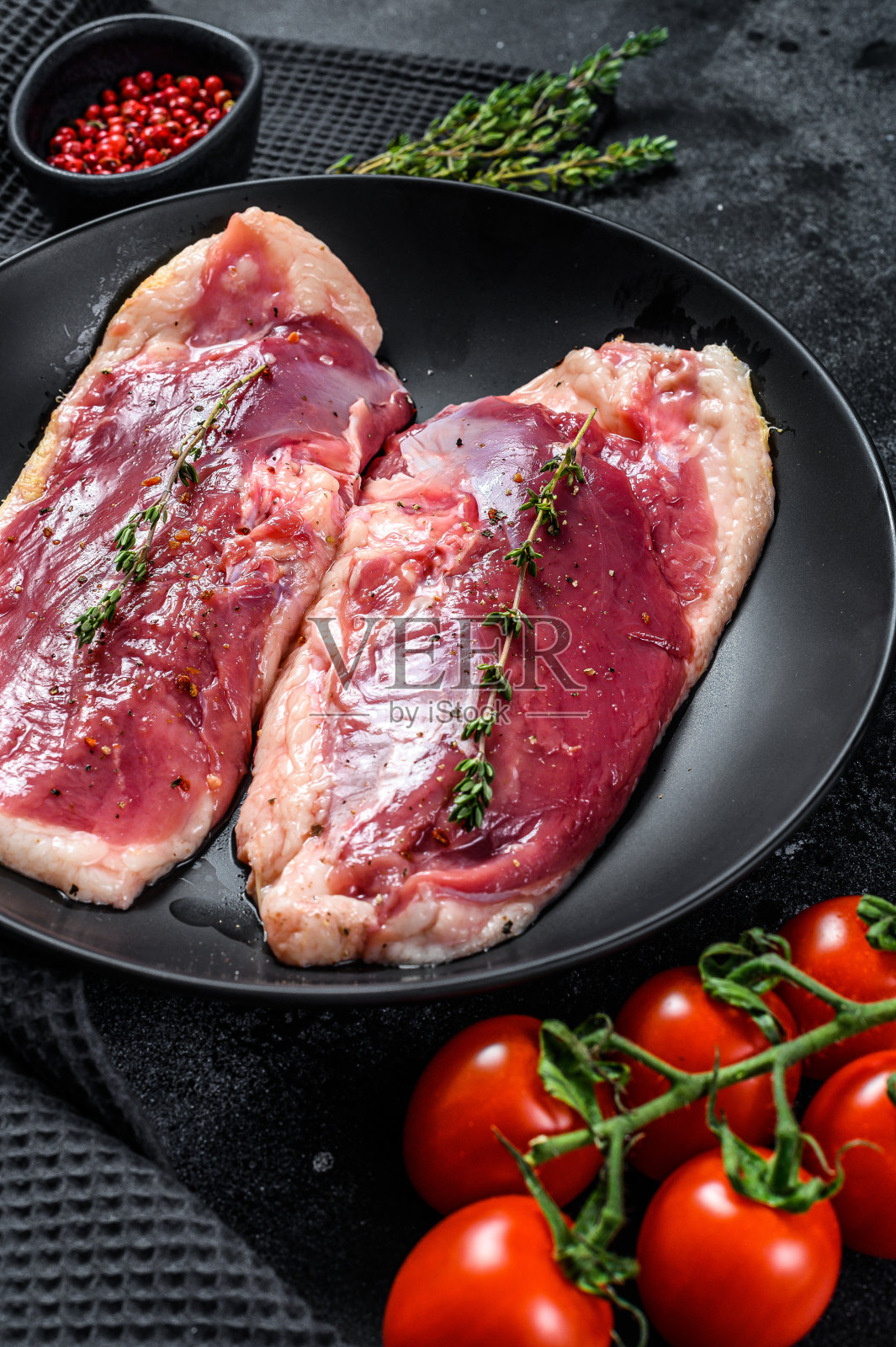 生鸭胸放在盘子里。有机禽肉。黑色背景。俯视图照片摄影图片