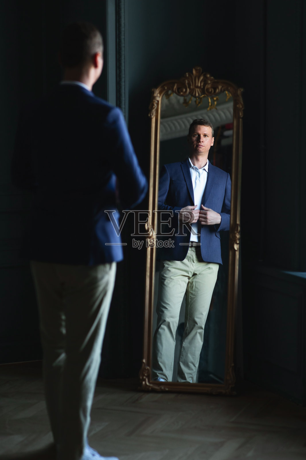 帅气时髦的男人穿着蓝夹克在家照镜子。照片摄影图片