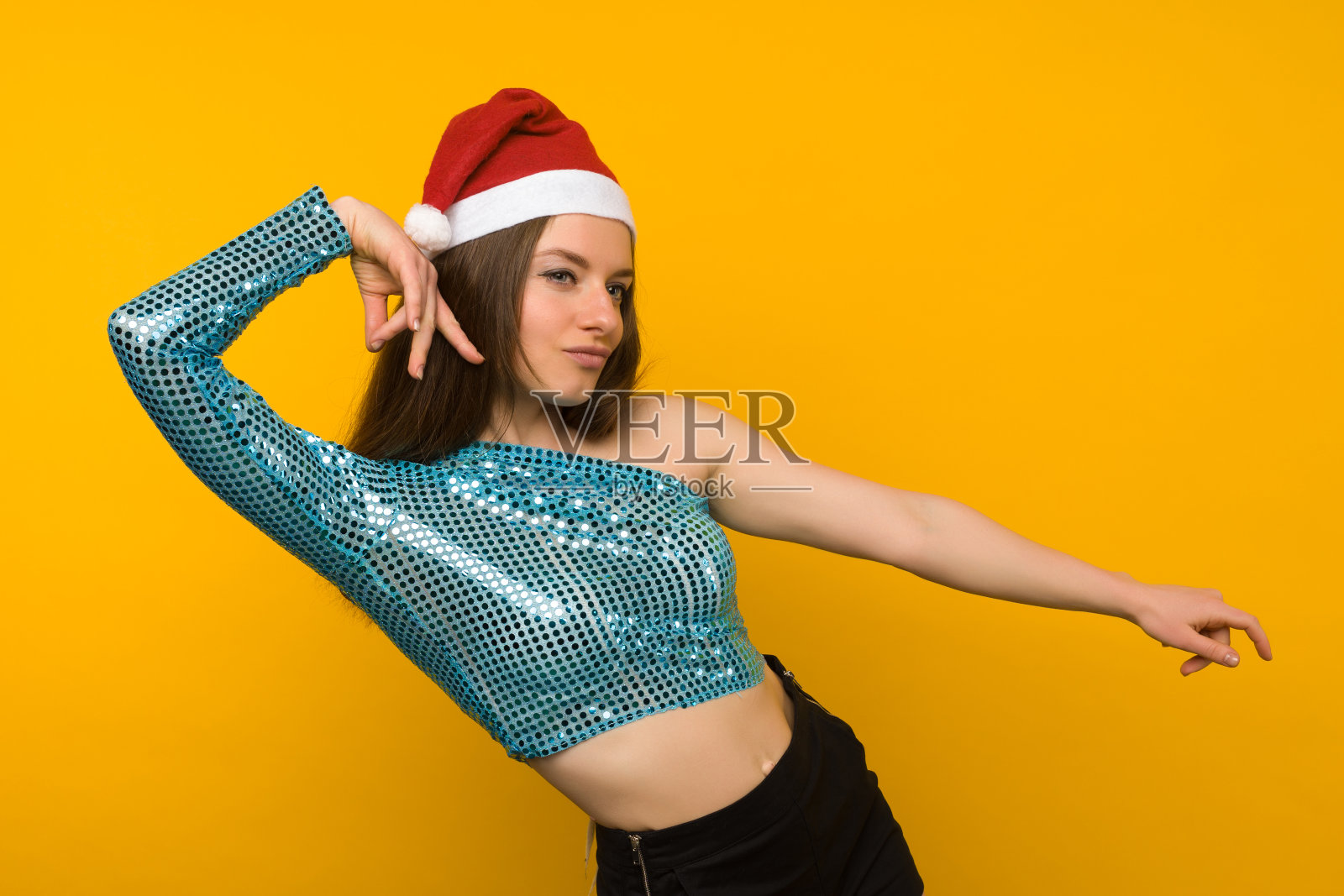 快乐的女孩在黄色的背景上戴着圣诞帽跳舞照片摄影图片