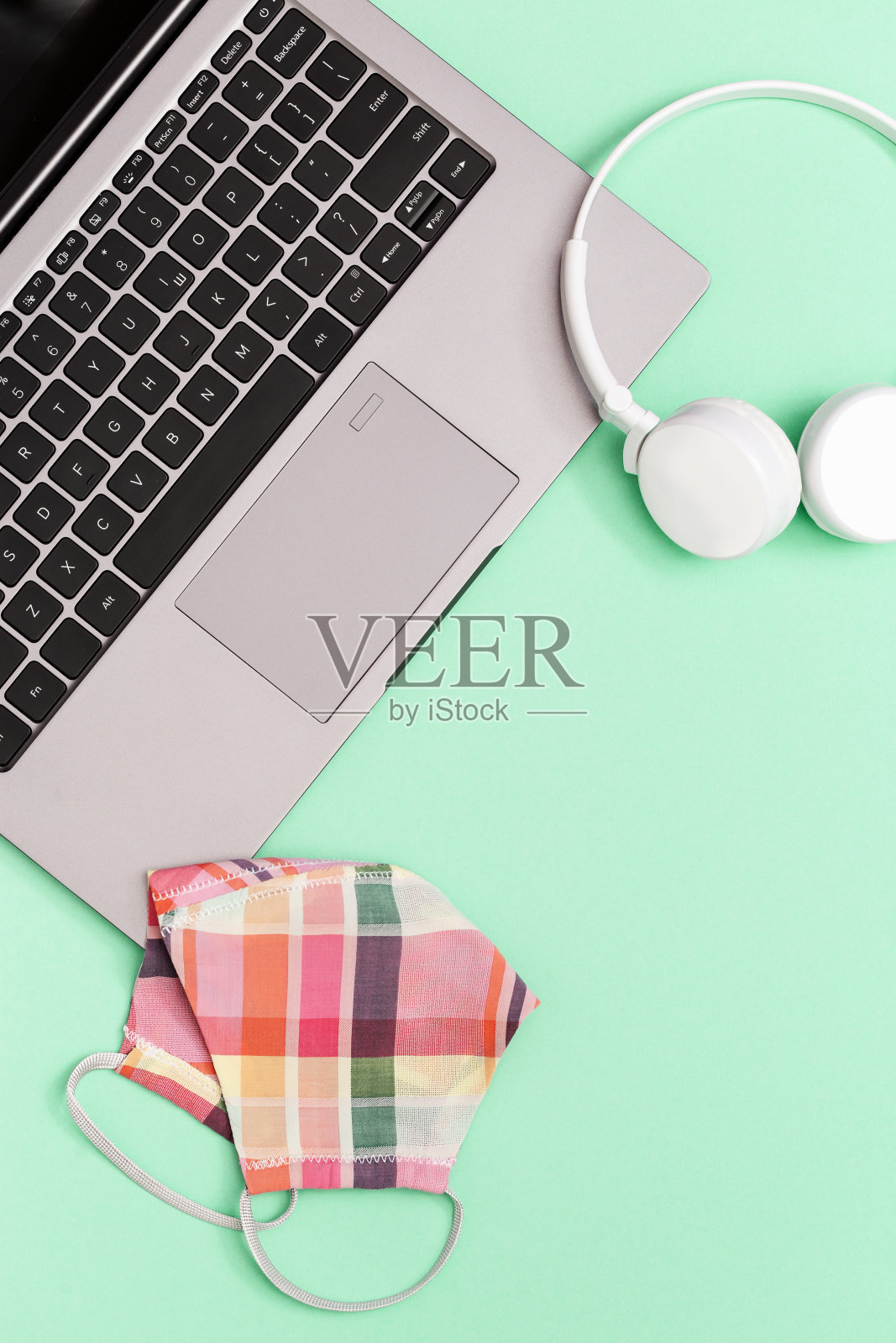 有灰色笔记本电脑和个人防护设备的工作或学习空间。用粉红色的布做医用口罩，以绿色的纸为背景。靠近，复制空间，平铺。照片摄影图片