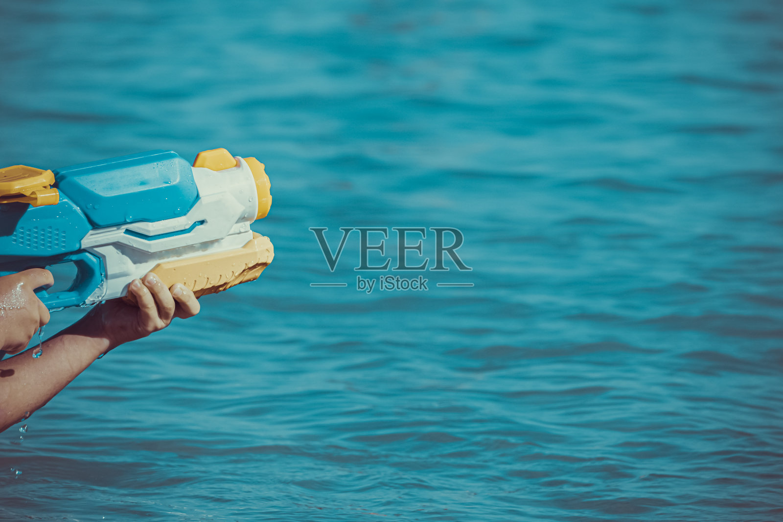 在夏日的阳光下，在海里玩水枪玩具。照片摄影图片