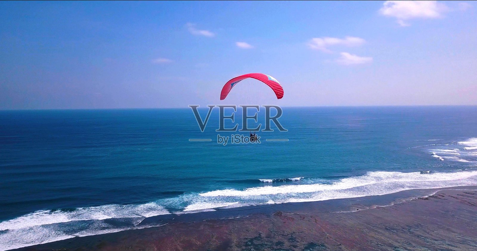 一张红色滑翔伞在海洋上飞行的照片照片摄影图片